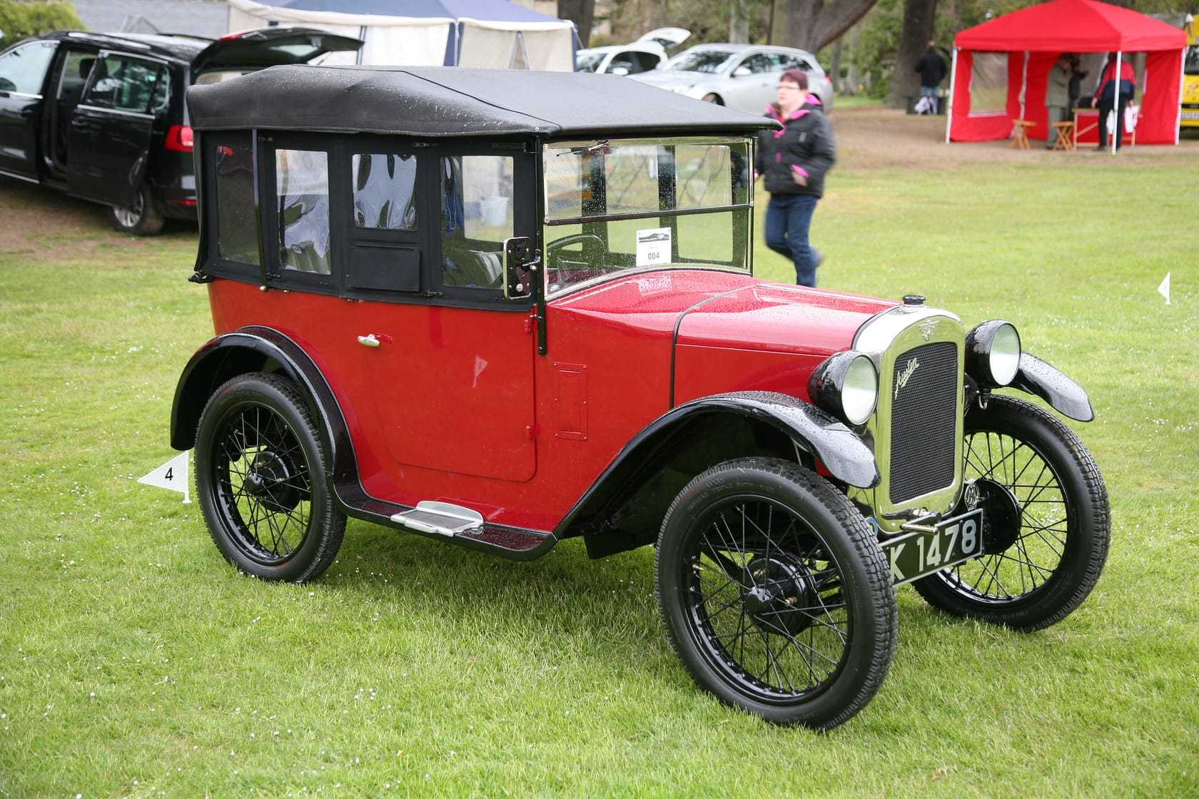 A red and black 1928 Austin Seven Chummy tourer with its hood up and a UK registration on a show field