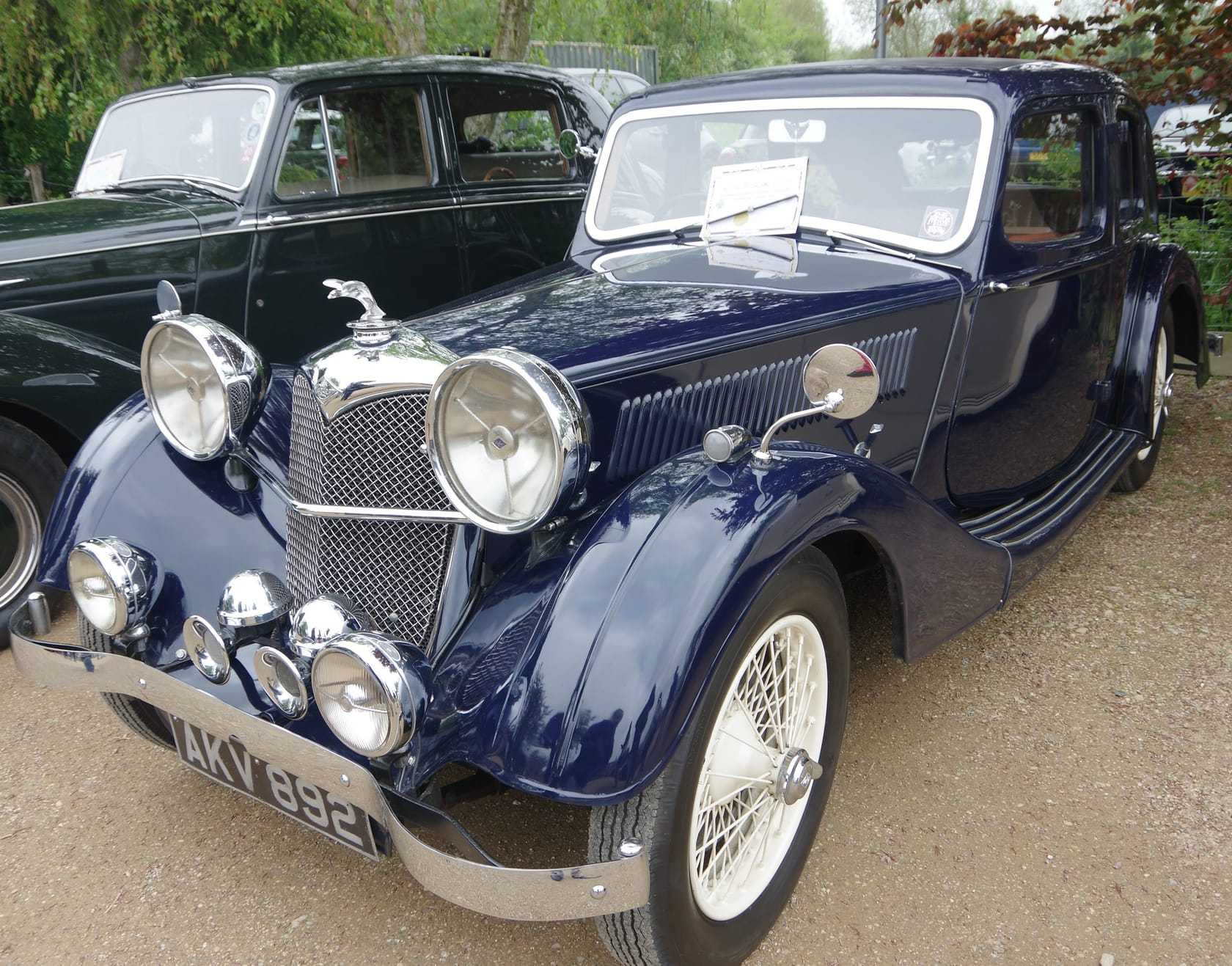 A dark blue 1936 Riley Kestrel fastback saloon with spot lamps at a classic car show, front three-quarter view