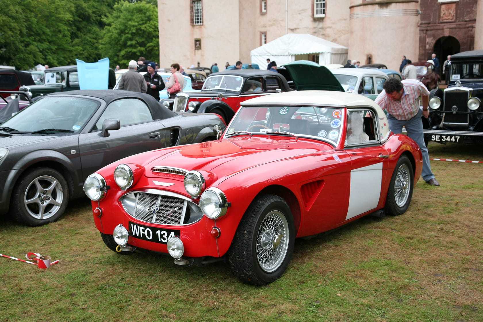 A red Austin-Healey Big Healey with a white hardtop at a classic-car show