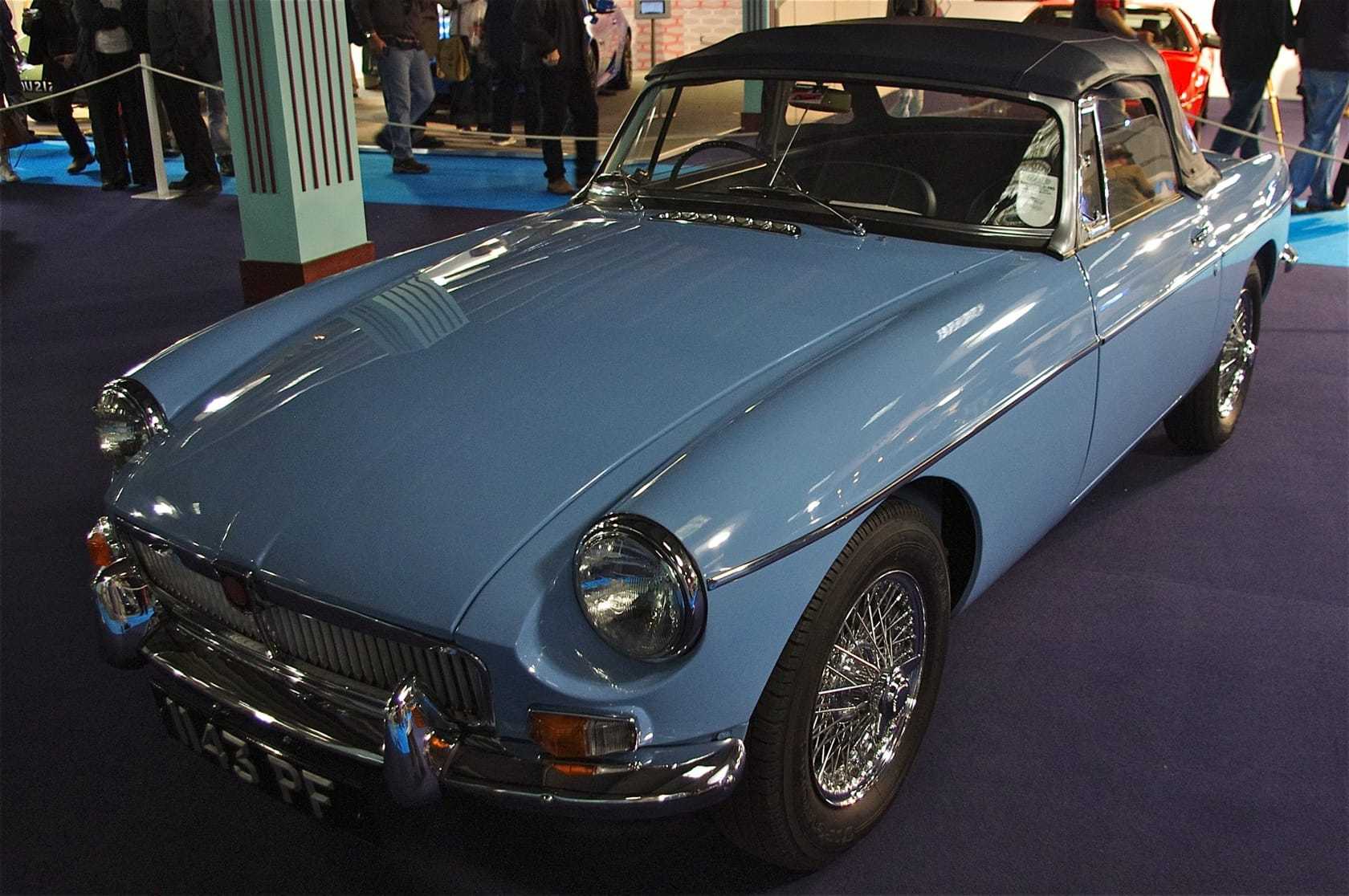 A pale blue early MGB roadster with chrome bumpers and wire wheels displayed indoors under lights