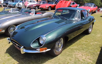 A row of Jaguar E-Types on a show field in Britain, a green Series 1 roadster with its hood down in front