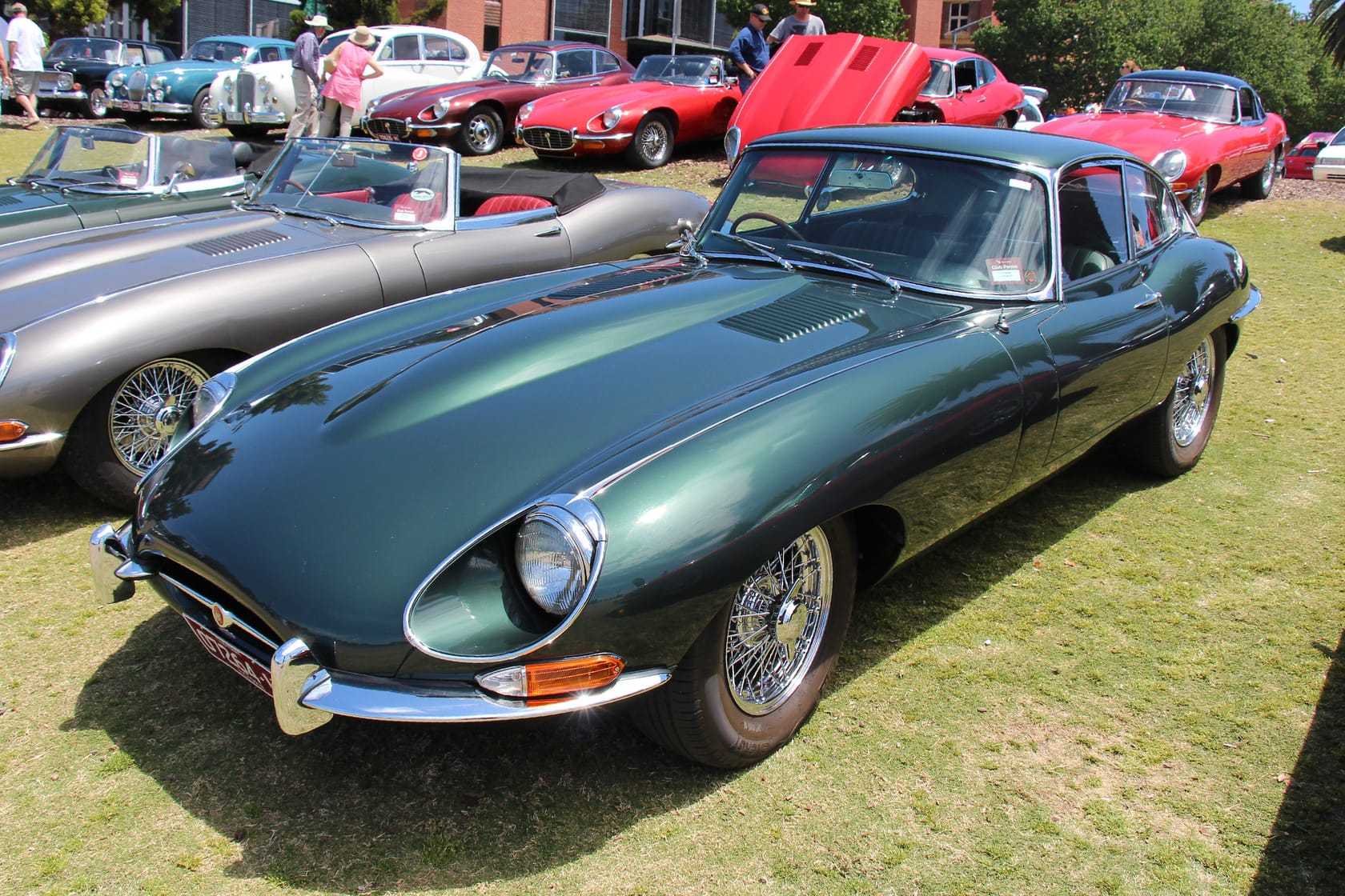 A row of Jaguar E-Types on a show field in Britain, a green Series 1 roadster with its hood down in front