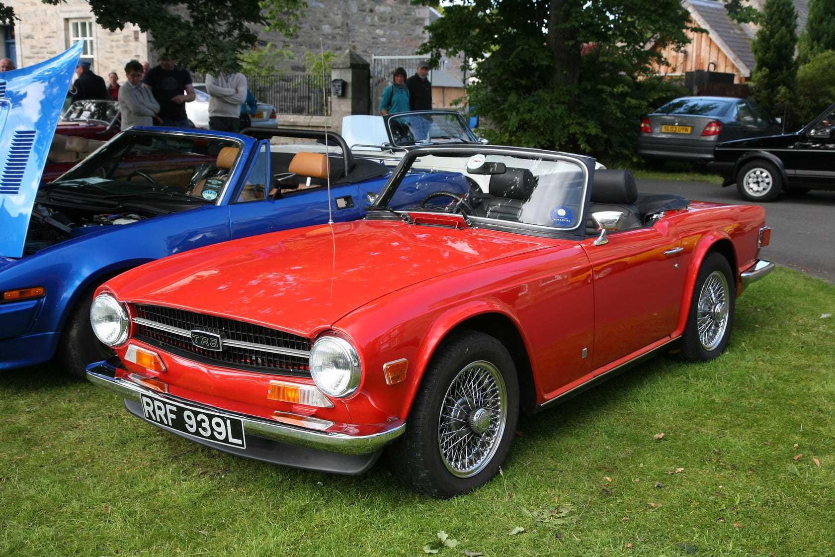A red 1972 Triumph TR6 with chrome wire wheels and a UK registration, parked on a show field with its hood down