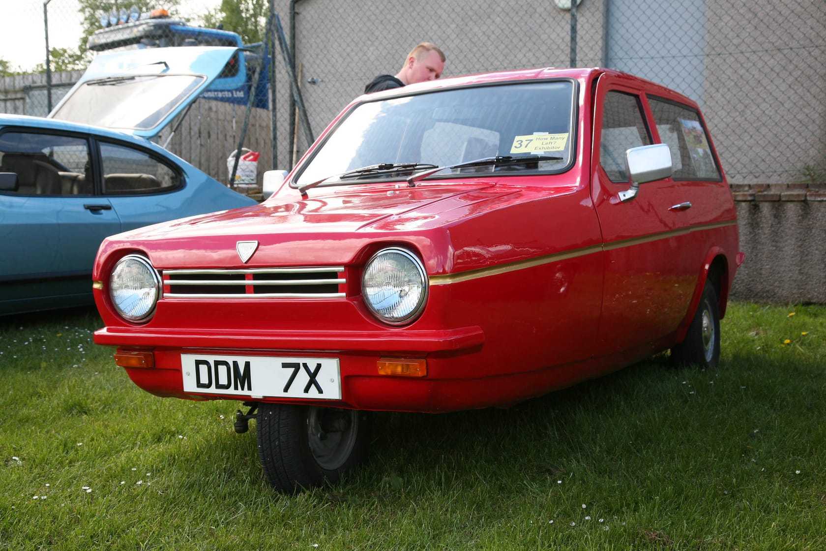 A red 1981 Reliant Robin Super on grass at a show, front three-quarter view, UK registration DDM 7X