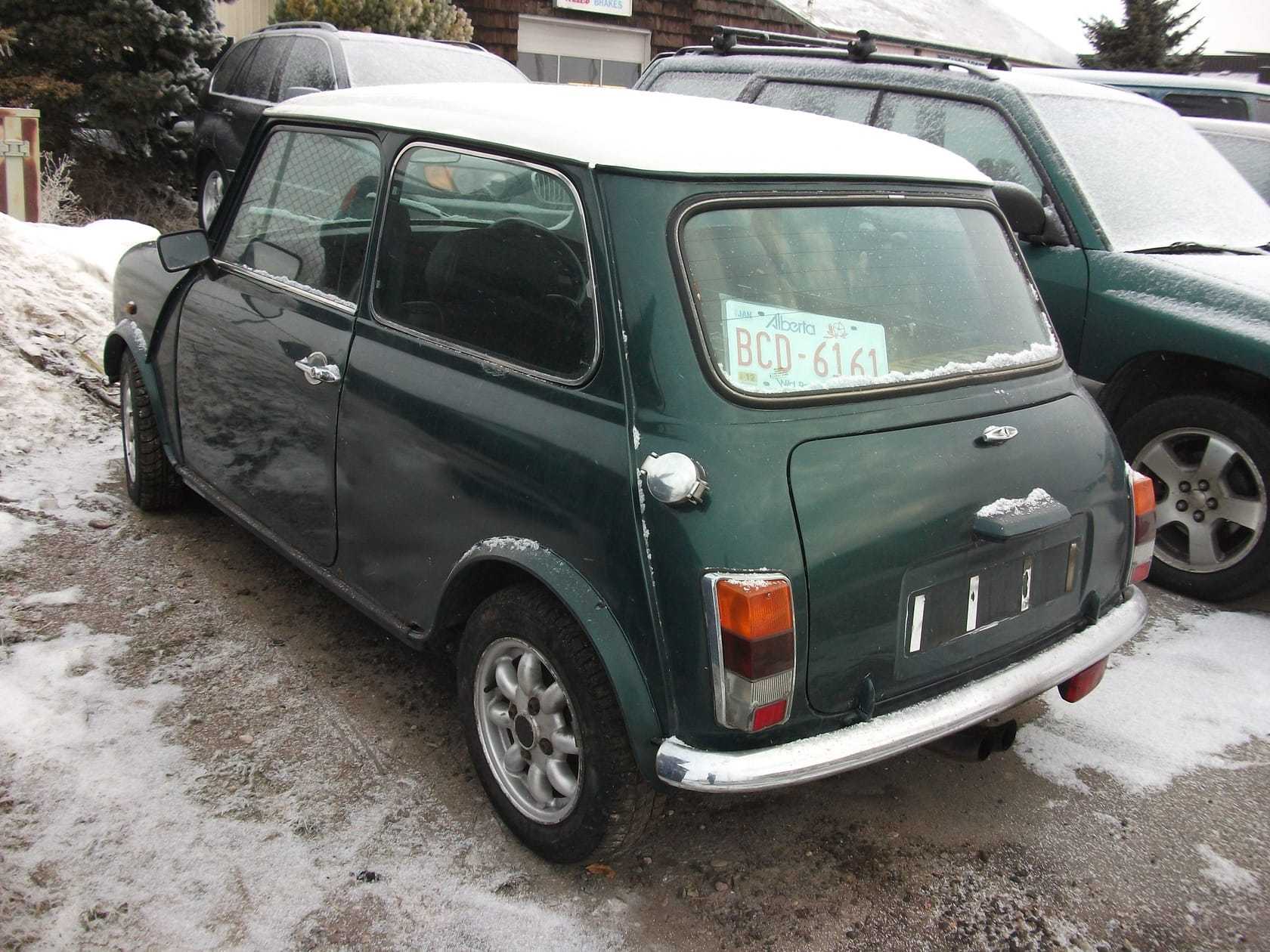 A dark green 1994 Rover Mini Cooper 1.3i with a white roof and bonnet stripes parked in a snowy car park