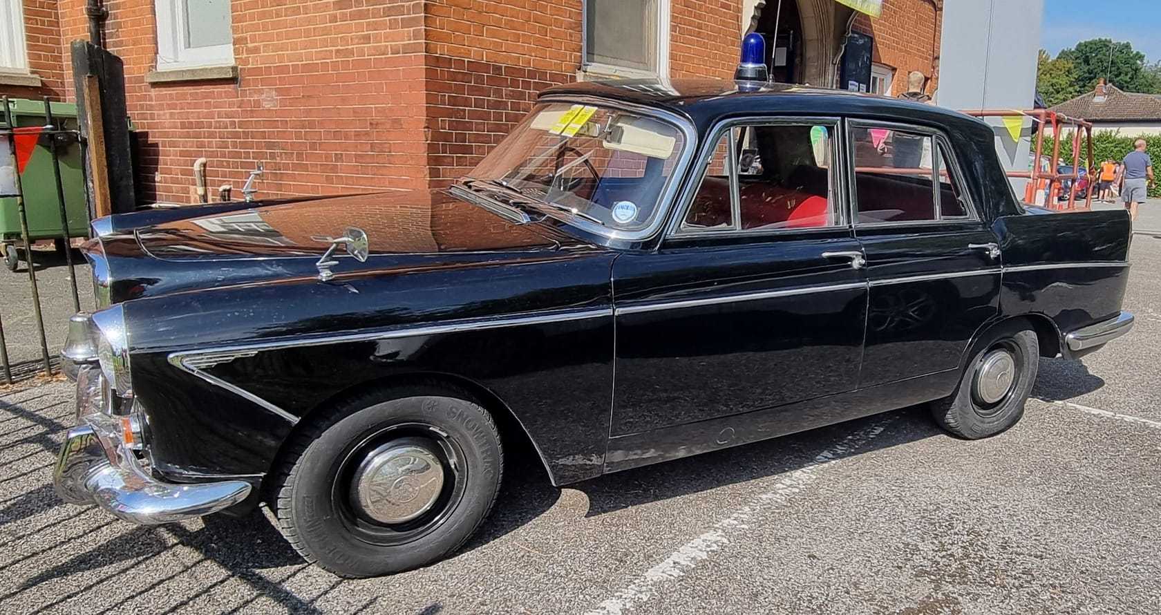 A black Wolseley 6/110 police car with blue light and police sign