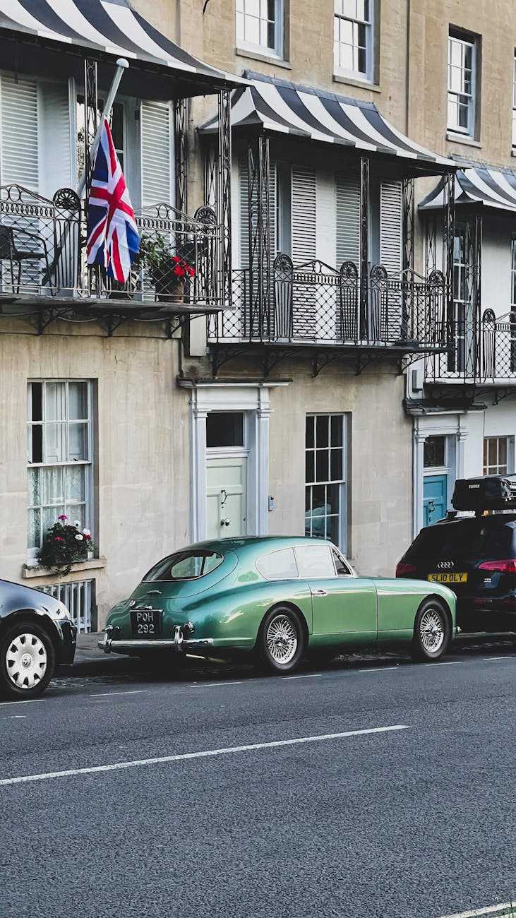 A green Aston Martin DB2/4 parked on a Regency street with a Union Jack flag behind