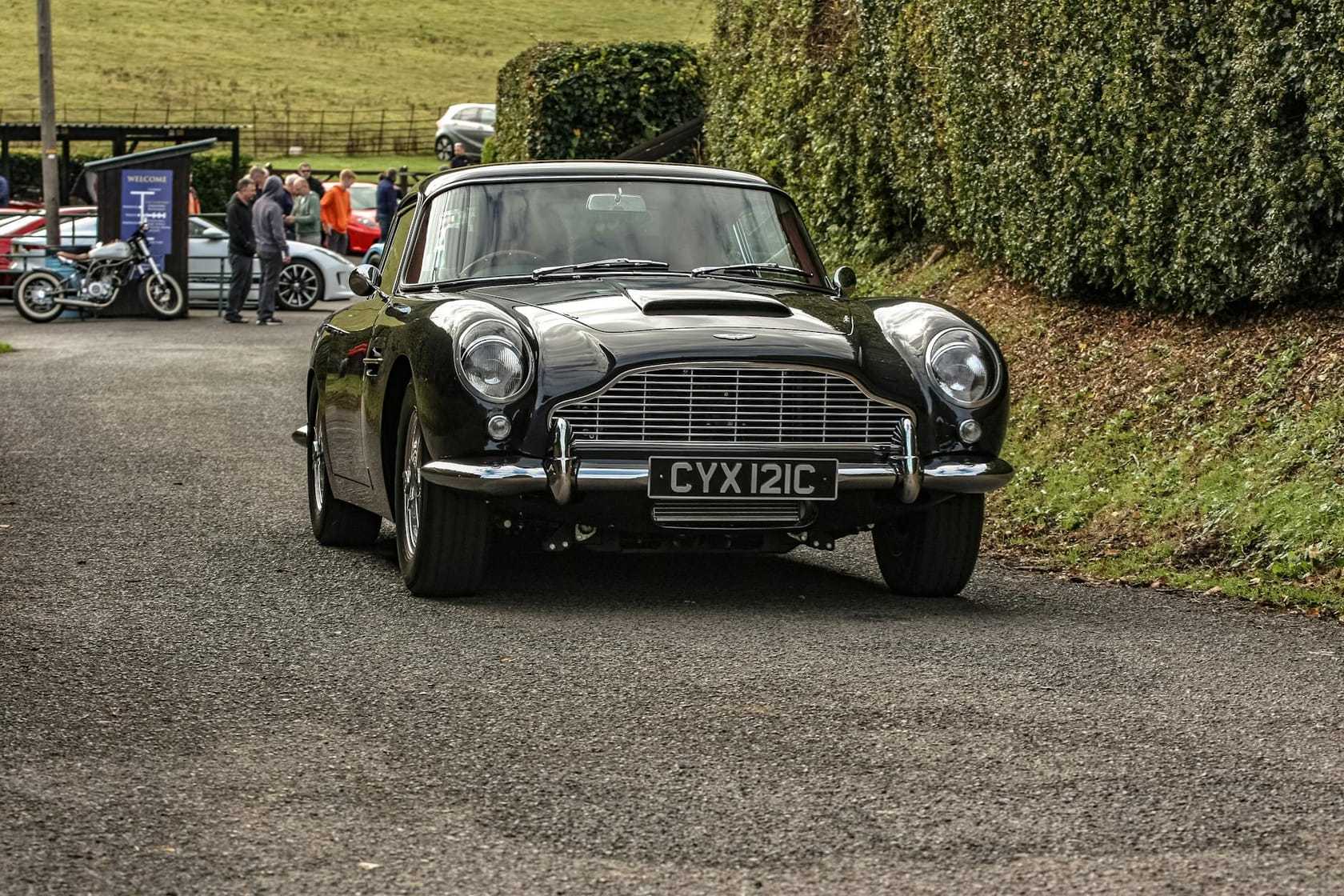 A black Aston Martin DB5 with UK registration CYX 121C photographed head-on against a hedge