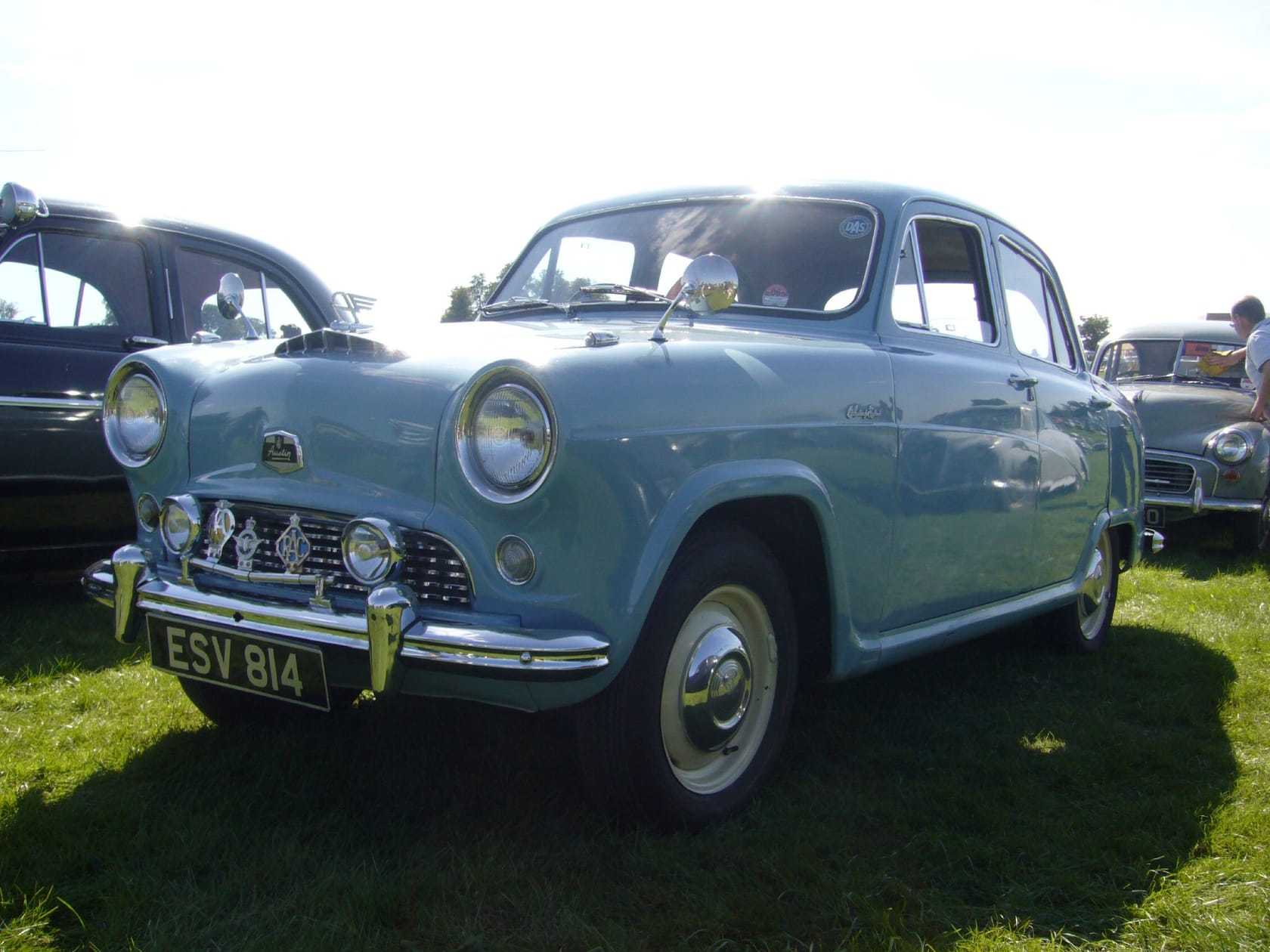 A light blue 1950s Austin saloon on grass at a classic car show, front three-quarter view, UK registration FSV 814