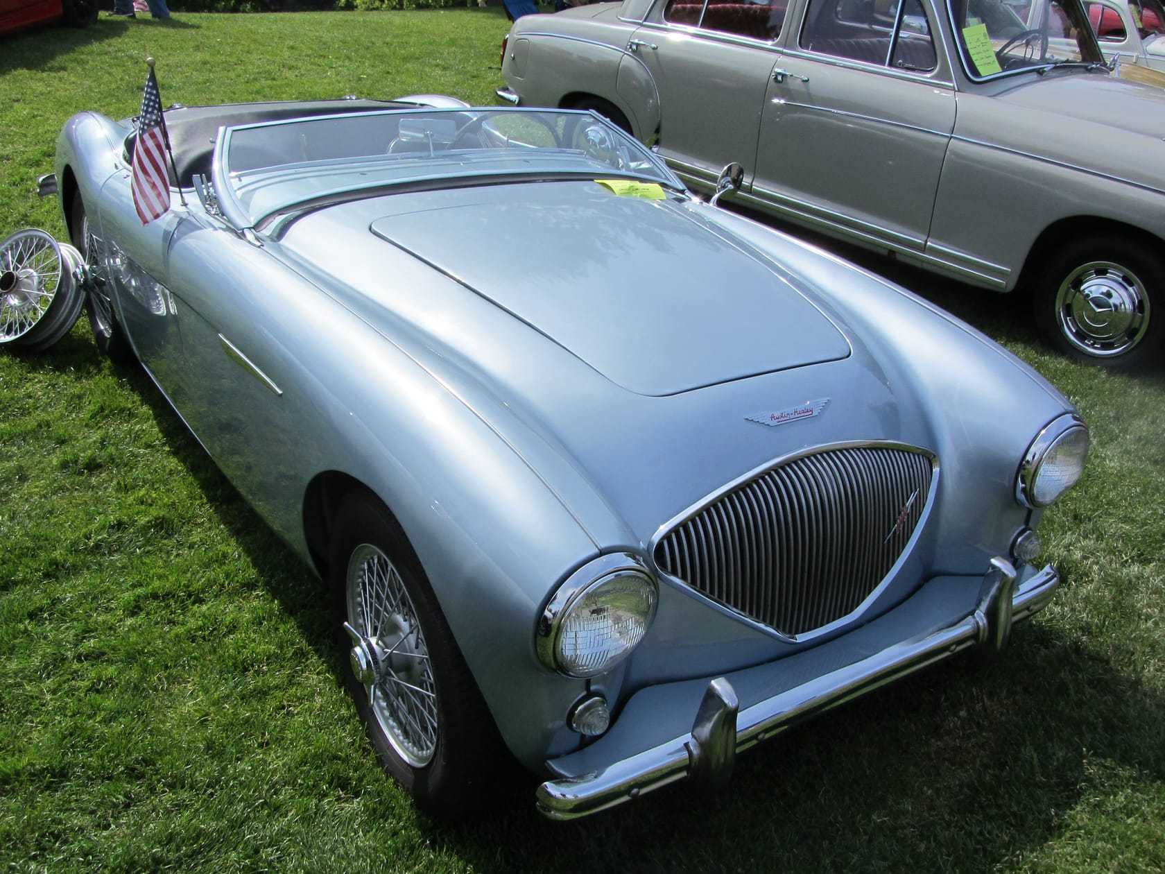 A silver-blue Austin-Healey 100 four-cylinder roadster, front three-quarter view, on show grass