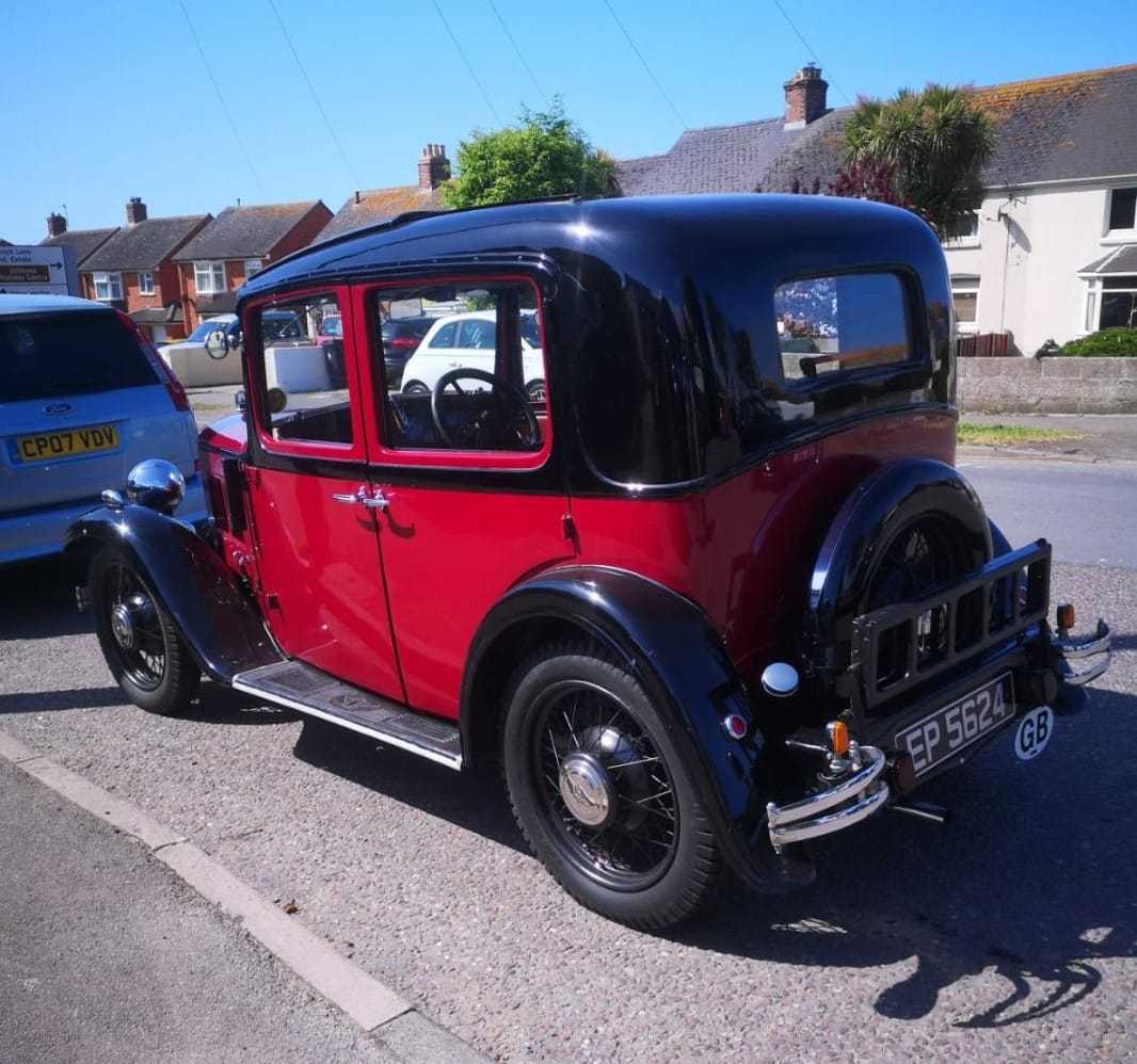 A red and black 1933 Austin Ten saloon parked on a suburban street, front three-quarter view