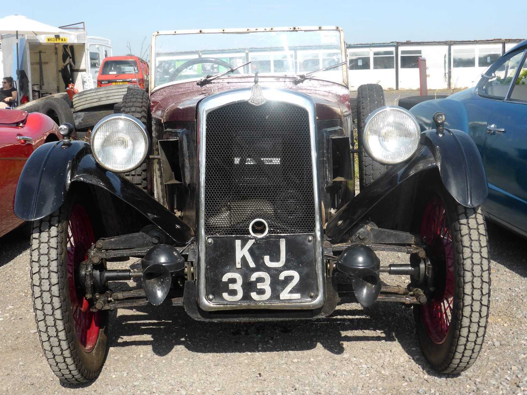 The front of a maroon and black 1931 BSA three-wheeler showing its v-twin engine and radiator, UK registration KJ 332