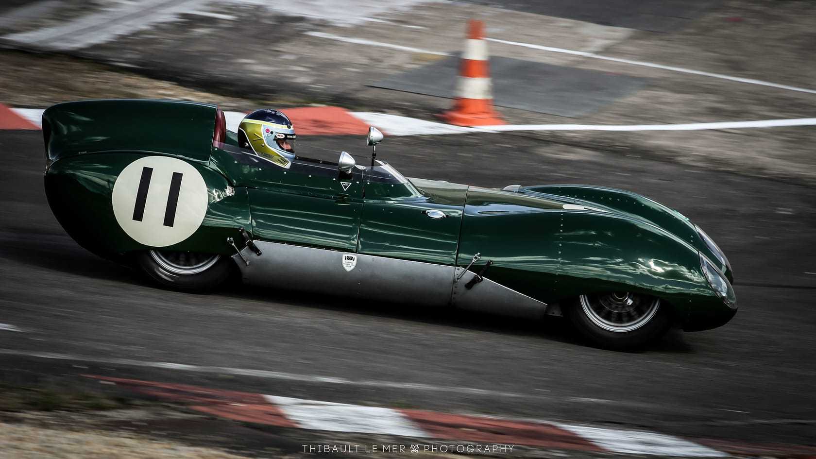 A green Lotus Eleven racing on a circuit, numbered 11, in a panned action shot