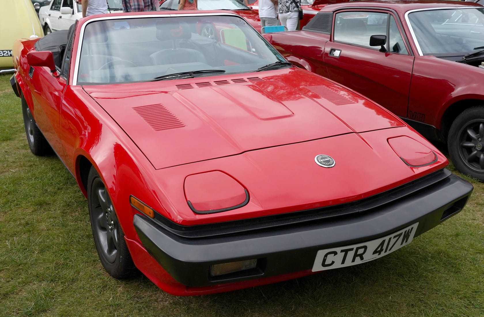 A red Triumph TR7 convertible with a UK registration parked on grass at a classic car show