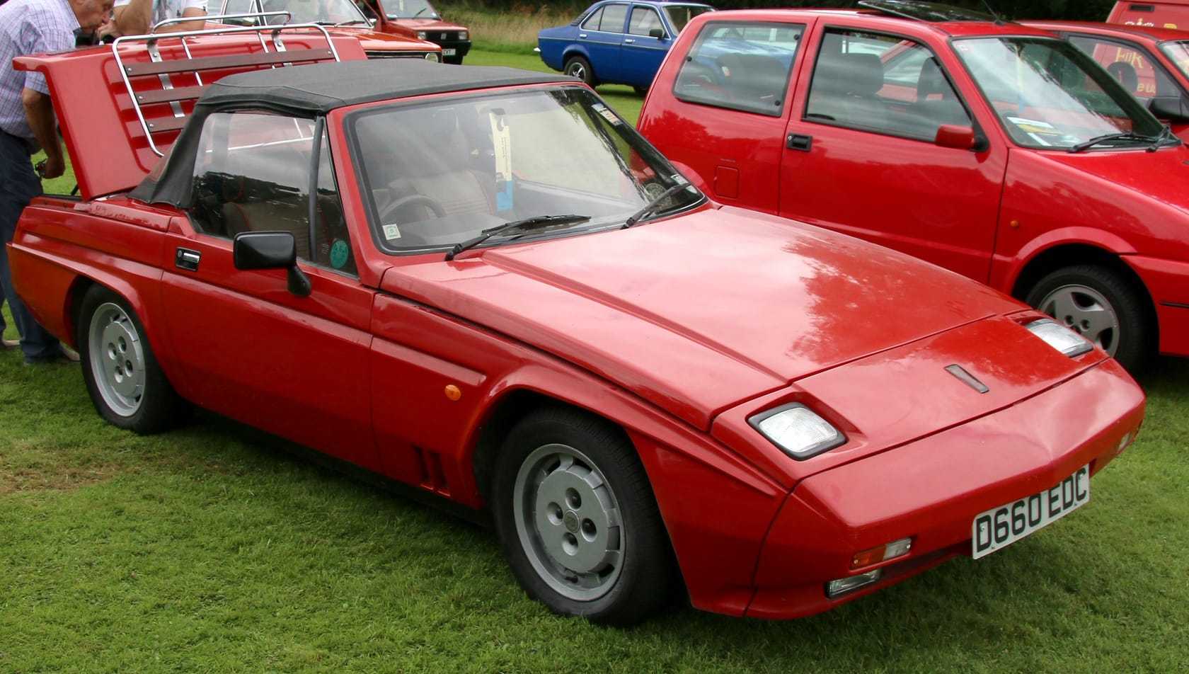 A red 1987 Reliant Scimitar SS1 with hardtop on a showfield, front three-quarter view, UK registration D660 EDC