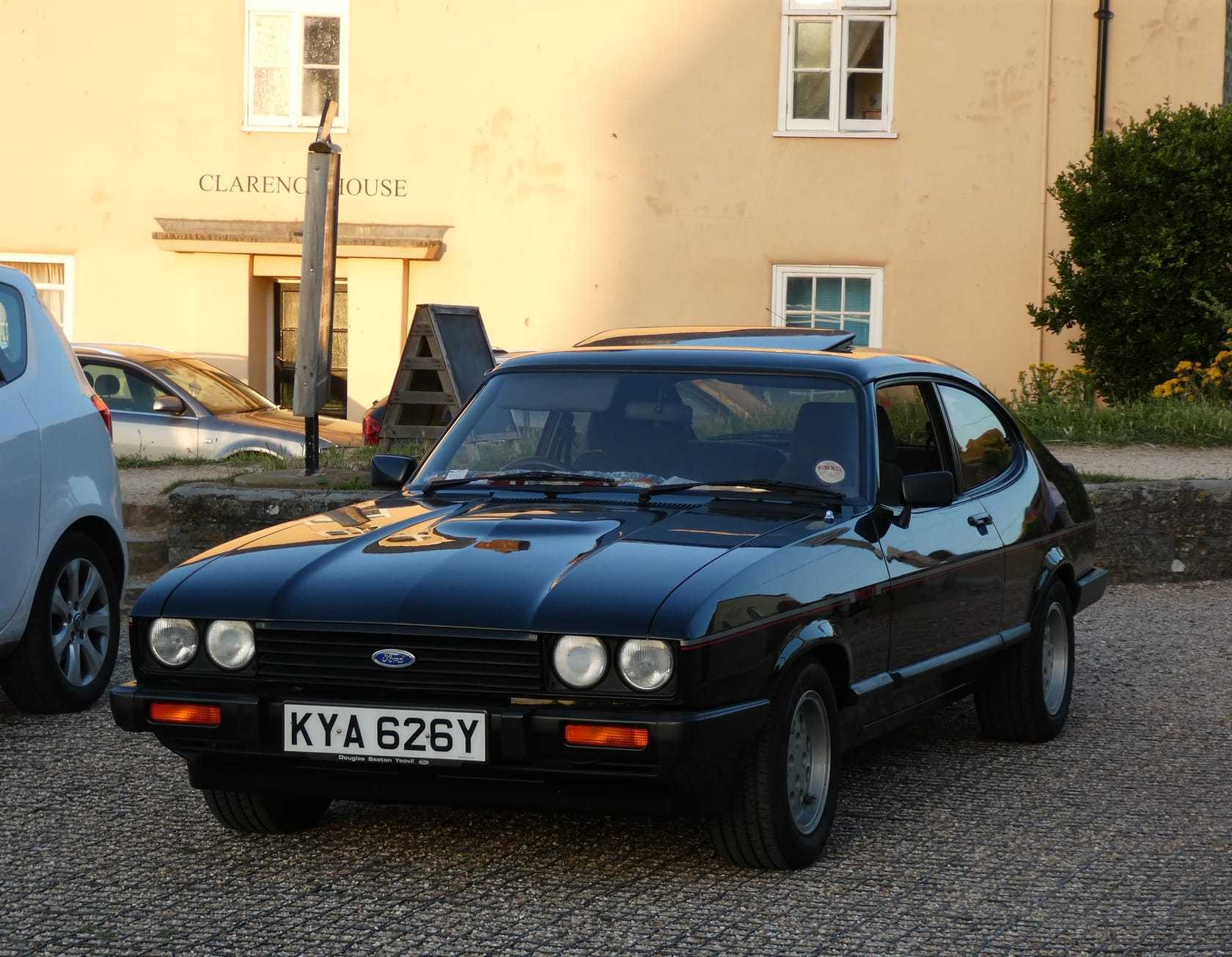 A black 1983 Ford Capri 2.8 Injection with a UK registration and pepperpot alloy wheels, parked outside a Georgian house