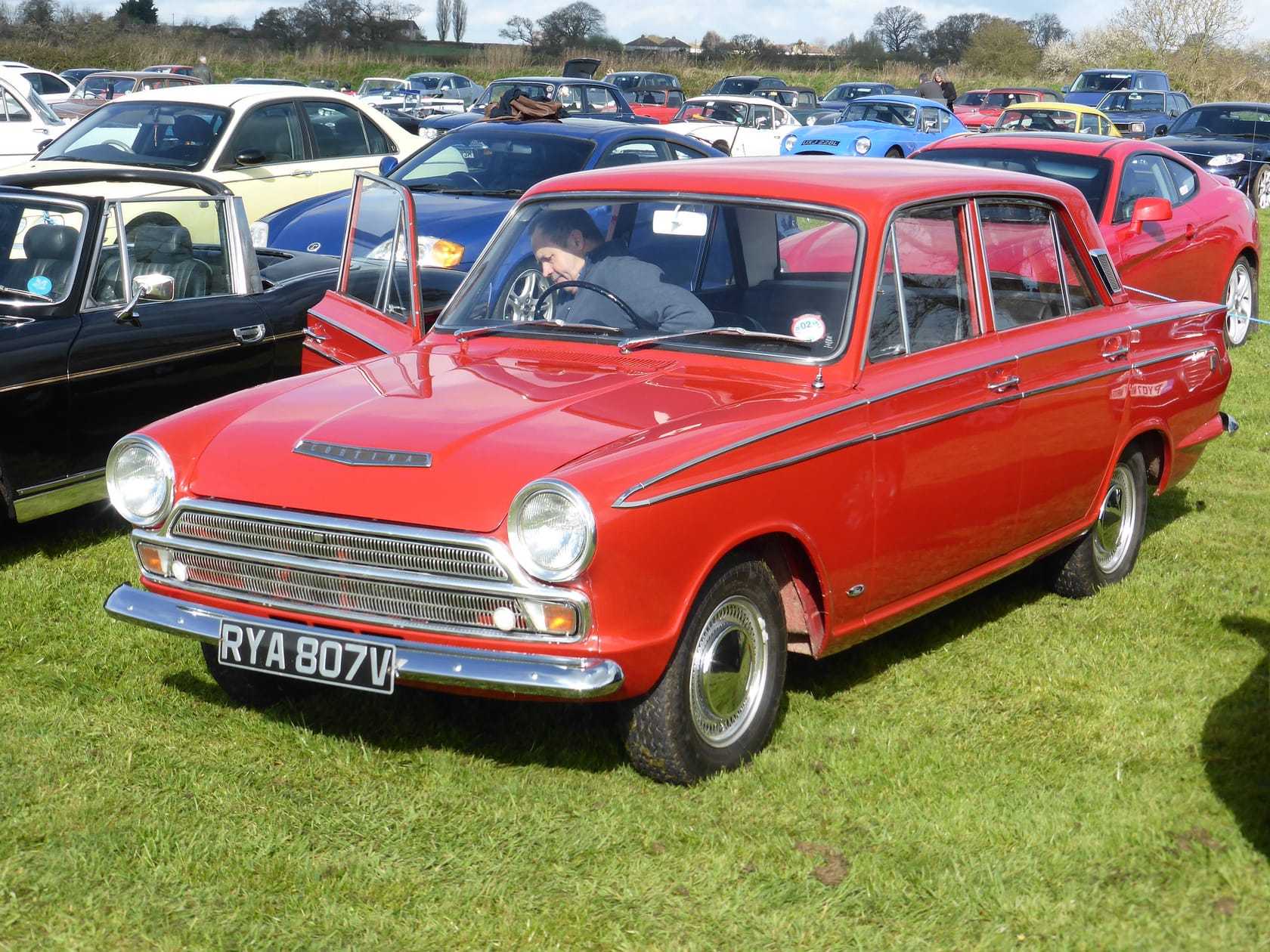 A red 1966 Ford Cortina Mk1 with UK registration RYA 807, front three-quarter view at a classic car show
