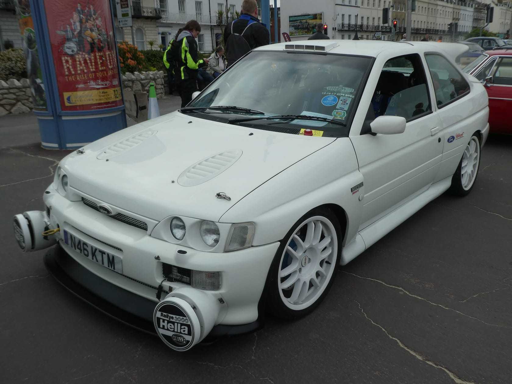 A white 1996 Ford Escort RS Cosworth with rally spot lamps at a seafront gathering, front three-quarter view