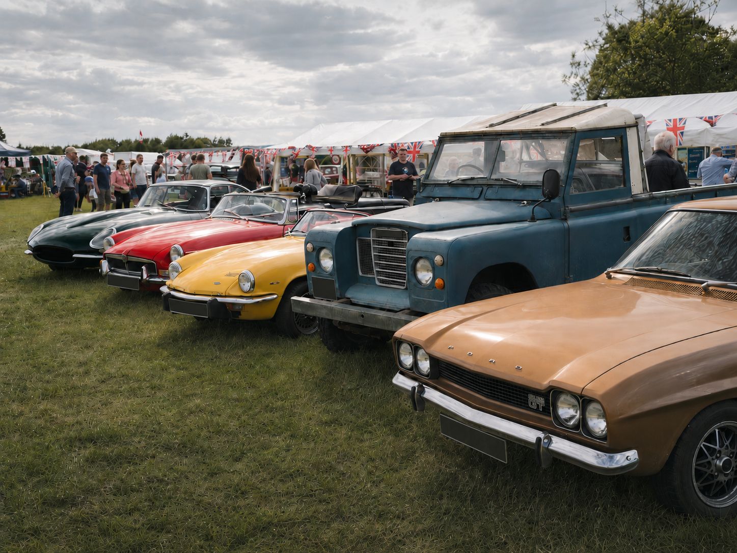 A line-up of British classics at a UK show — Jaguar E-Type, Triumph Spitfire, Bond Bug, Land Rover Series, and Ford Cortina visible