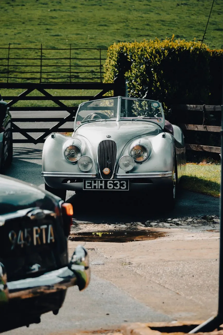 A silver Jaguar XK120 roadster parked by a stone wall, front three-quarter view
