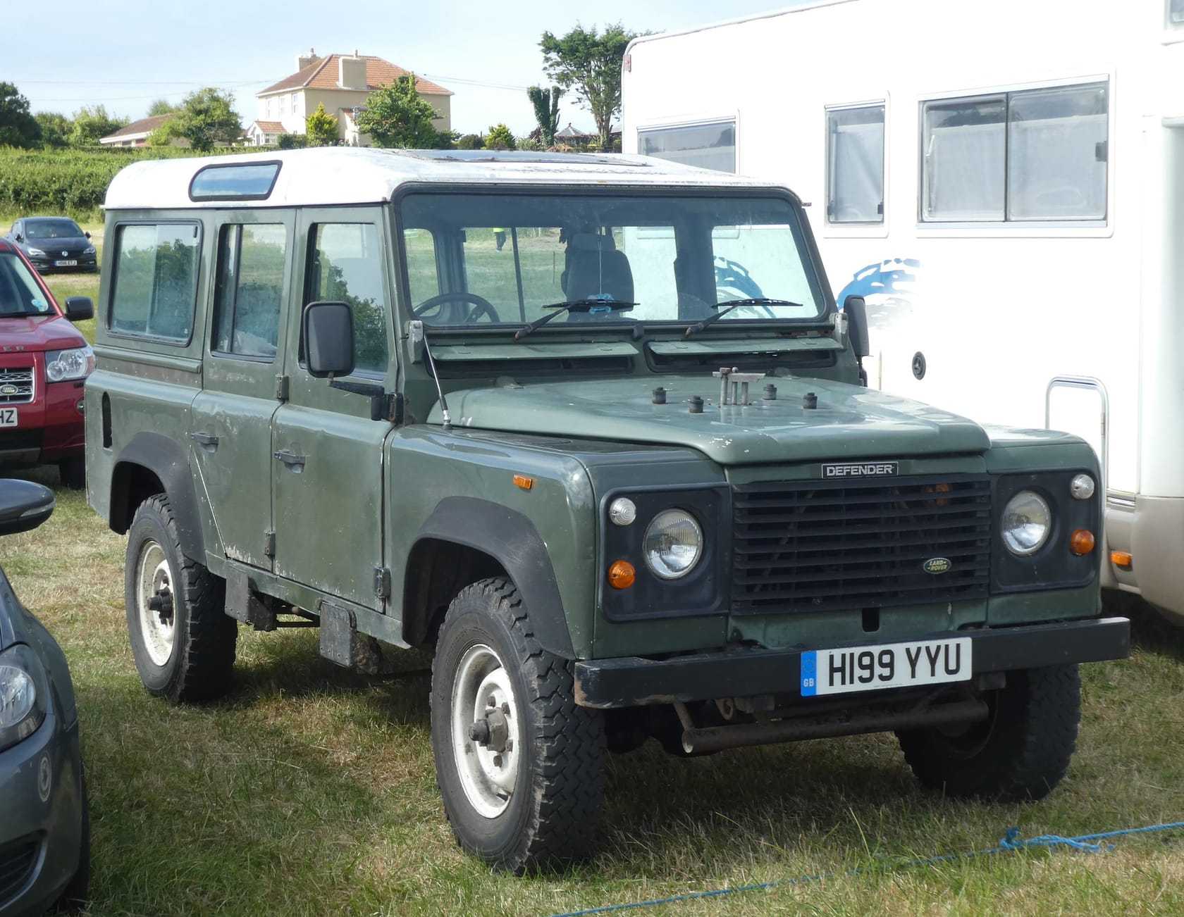 A green 1991 Land Rover Defender 110 station wagon with a UK registration parked on grass at a show