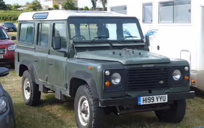 A green 1991 Land Rover Defender 110 station wagon with a UK registration parked on grass at a show