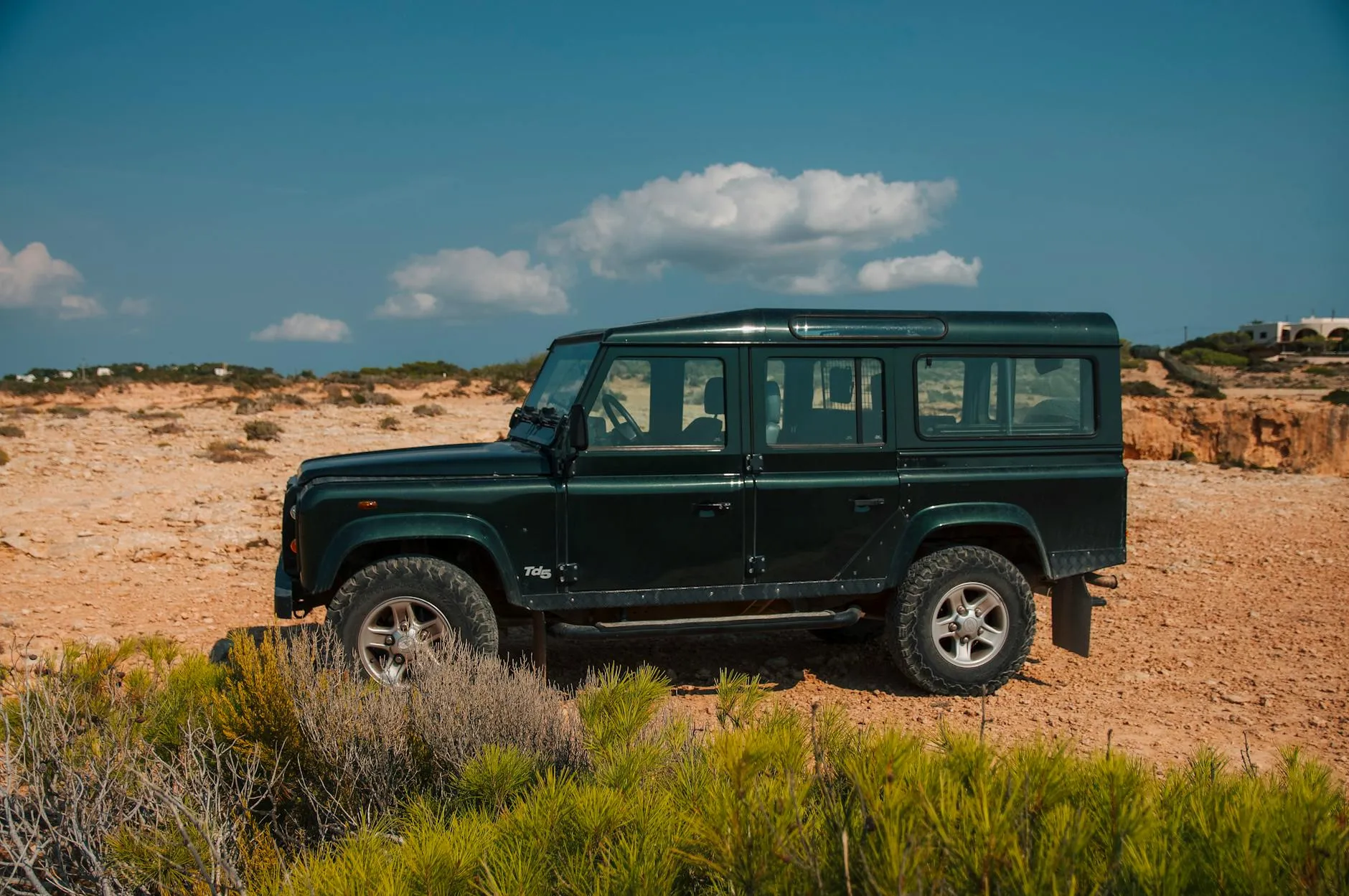 A green Land Rover Defender 110 parked on open scrubland under a blue sky