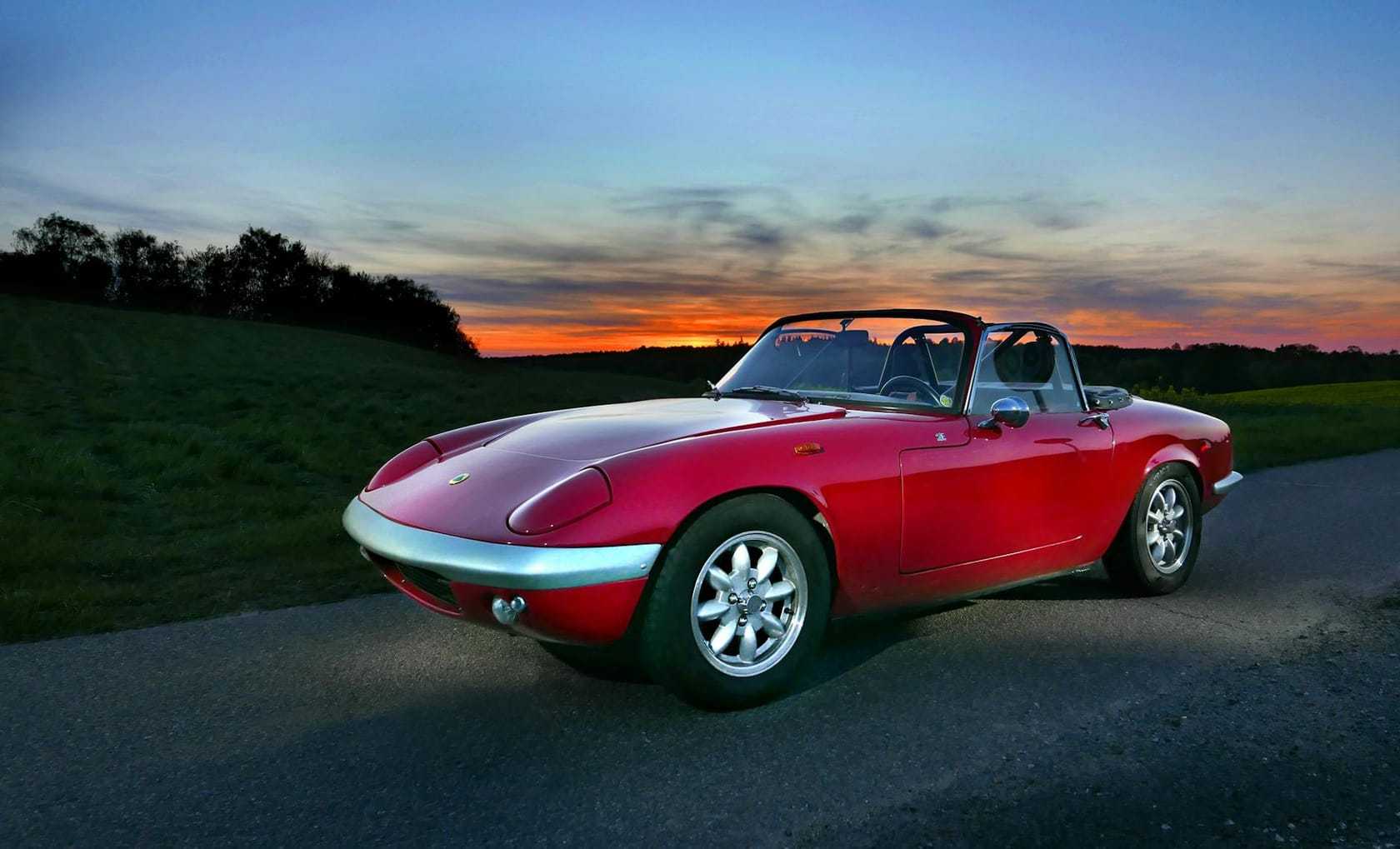 A red Lotus Elan roadster on a country road at sunset, front three-quarter view