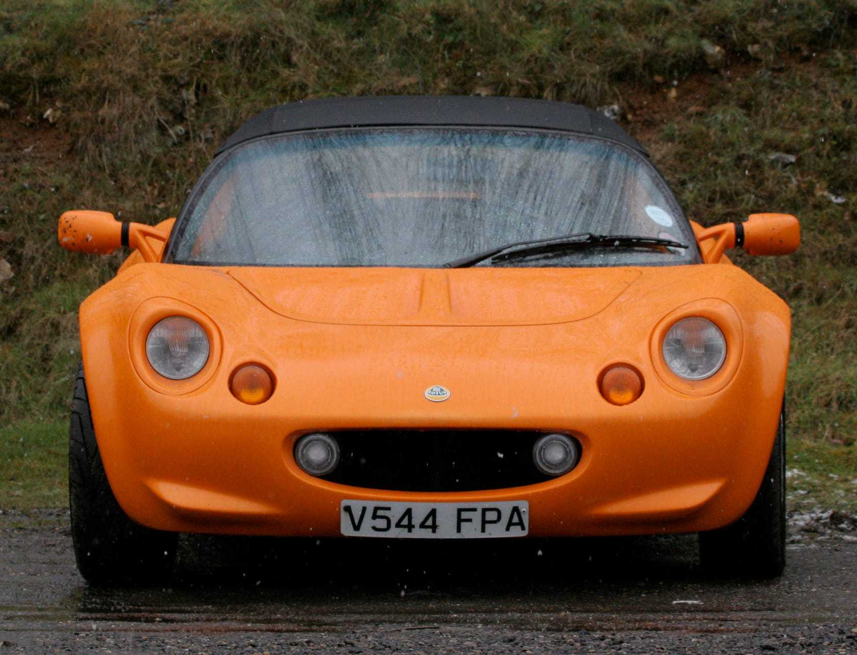 An orange Series 1 Lotus Elise photographed head-on, wearing a UK registration plate