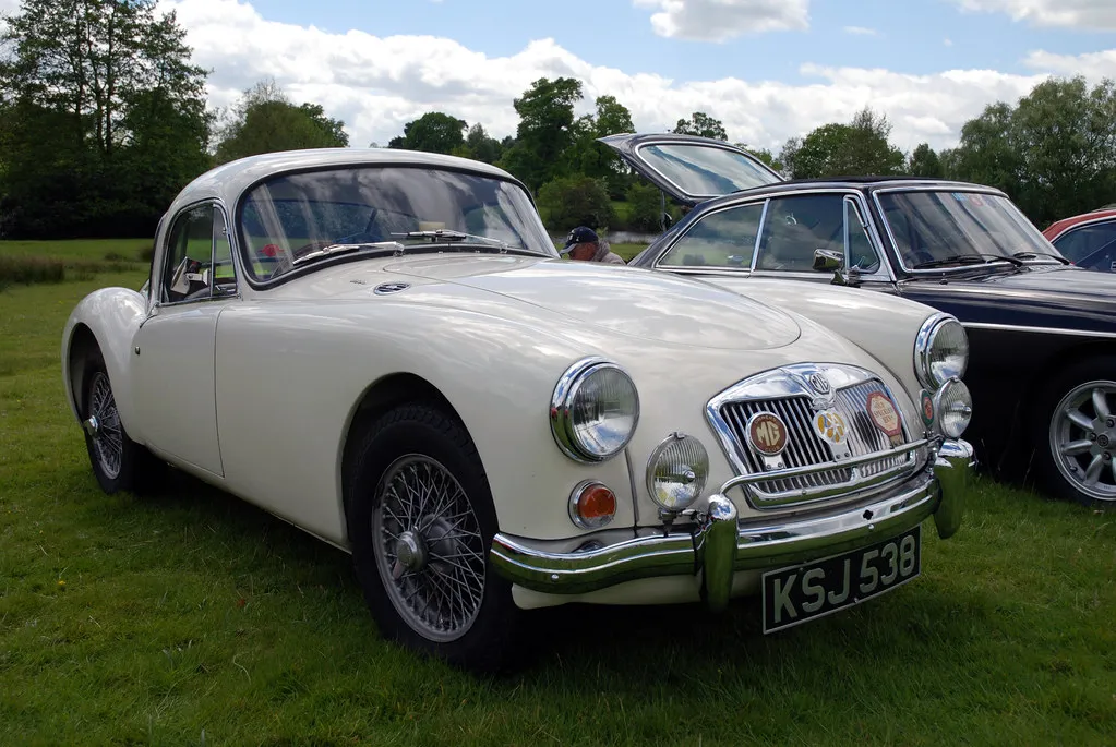 A cream MG MGA fixed-head coupe with wire wheels, front three-quarter view on grass at a classic car show