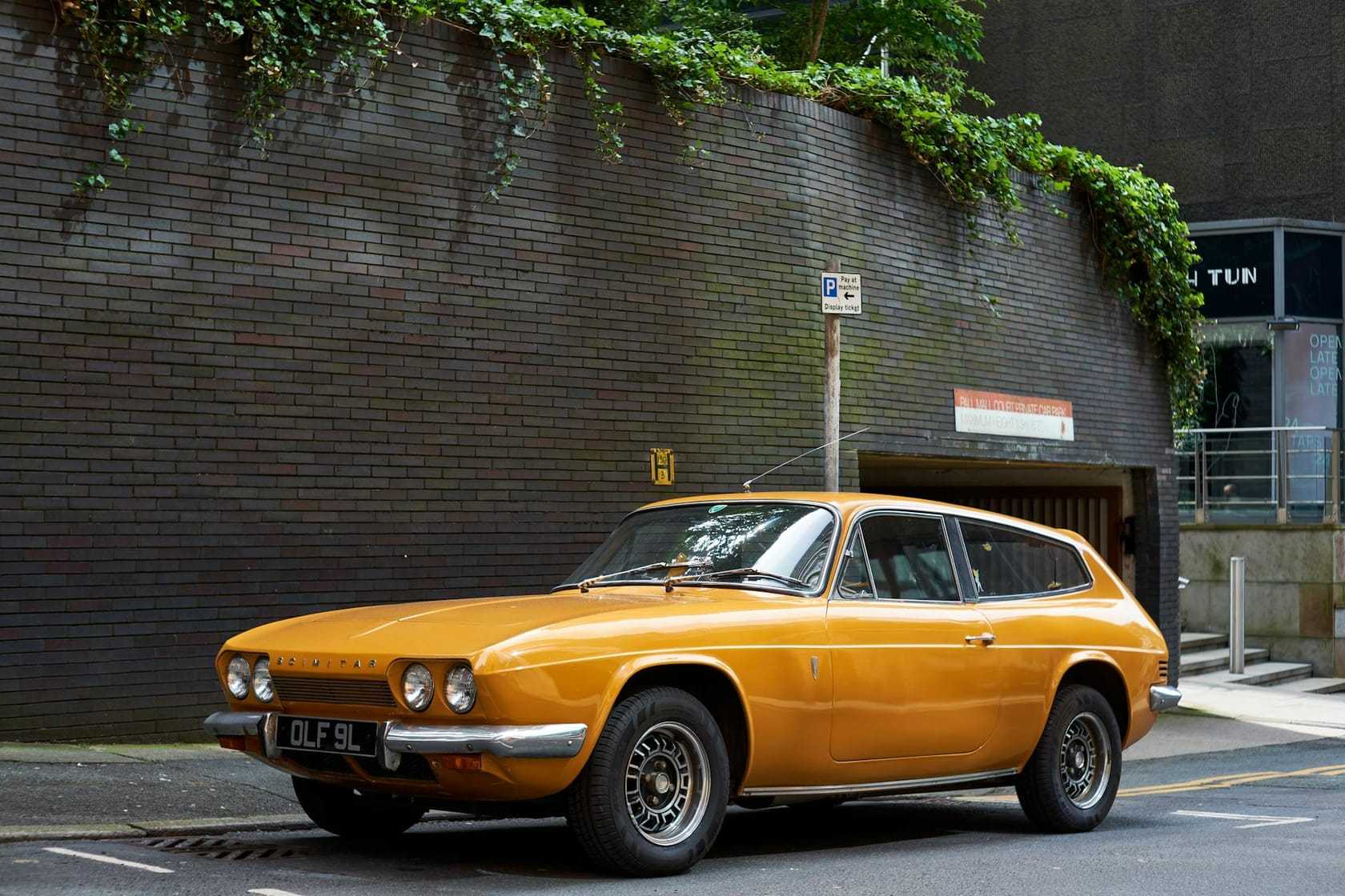 An orange Reliant Scimitar GTE parked on a street beneath an ivy-covered wall, side view