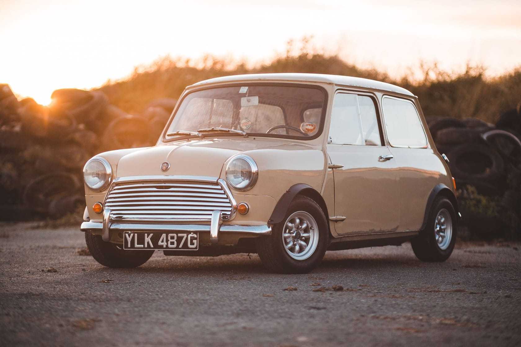 A cream classic Mini with a white roof, front three-quarter view at golden hour, registration YLK 487G