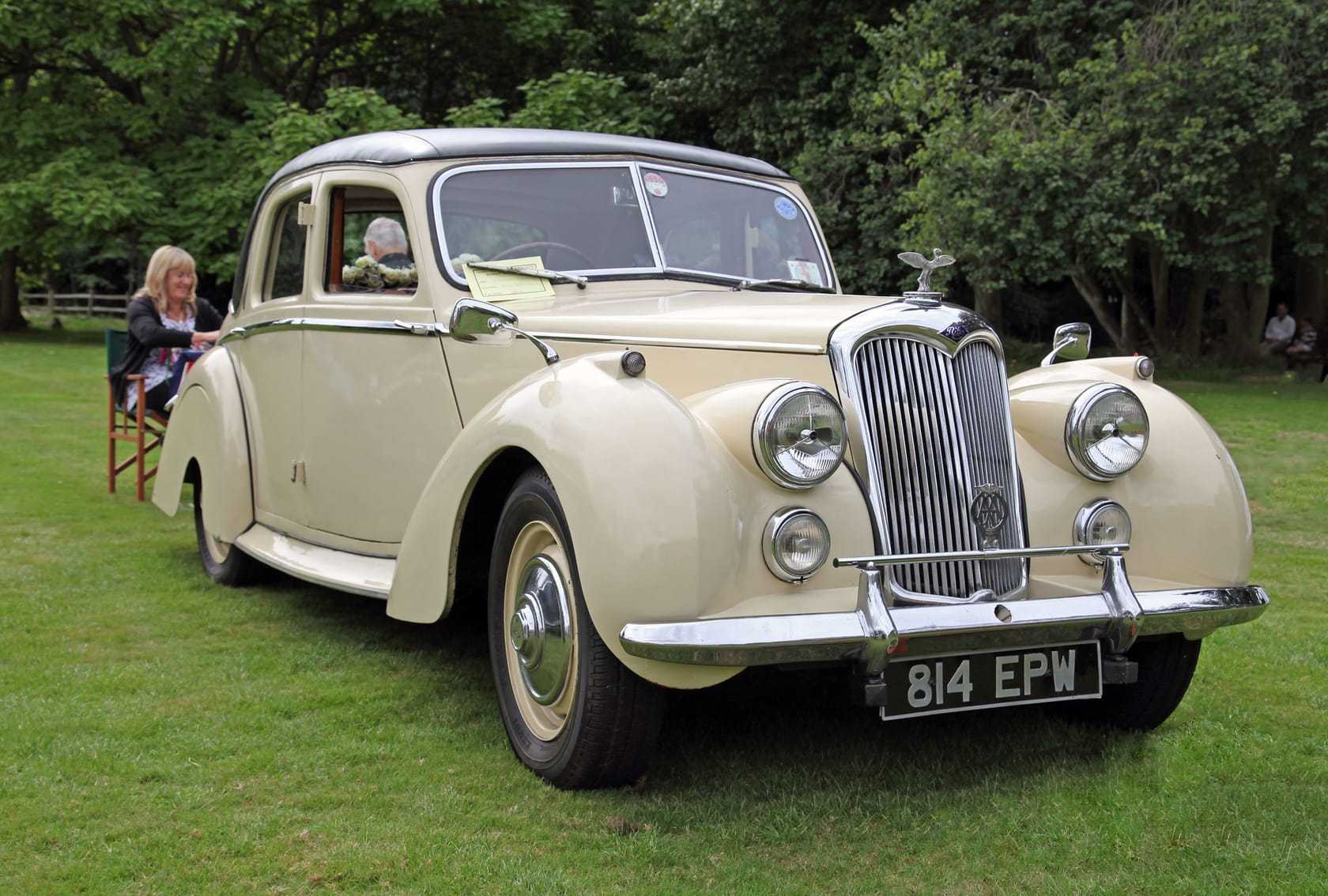 A cream 1954 Riley RME 1.5-litre saloon on grass at a classic car show, front three-quarter view, UK registration 814 EPW