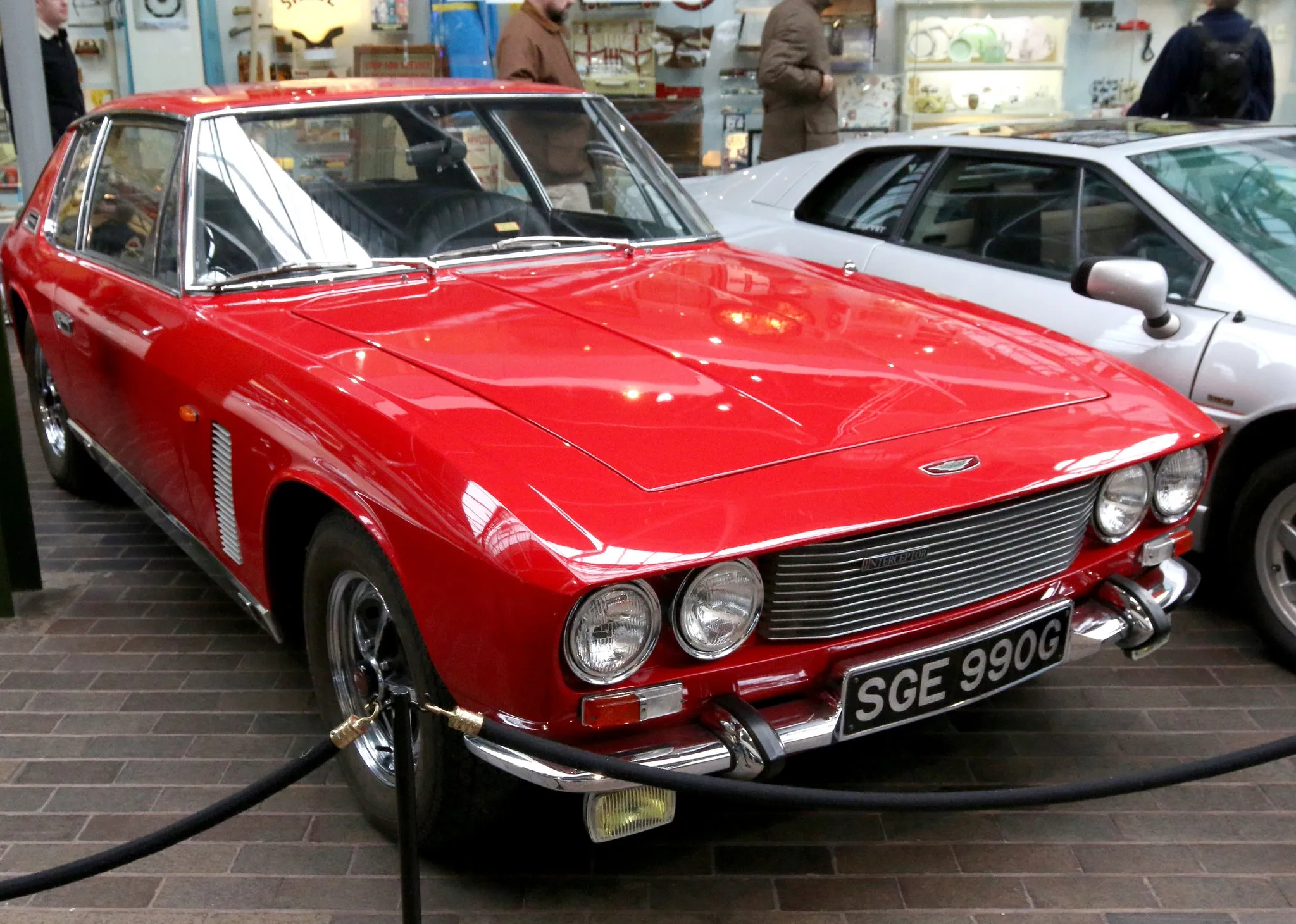 A red Jensen Interceptor at an indoor display, front three-quarter view, UK registration SGE 990G