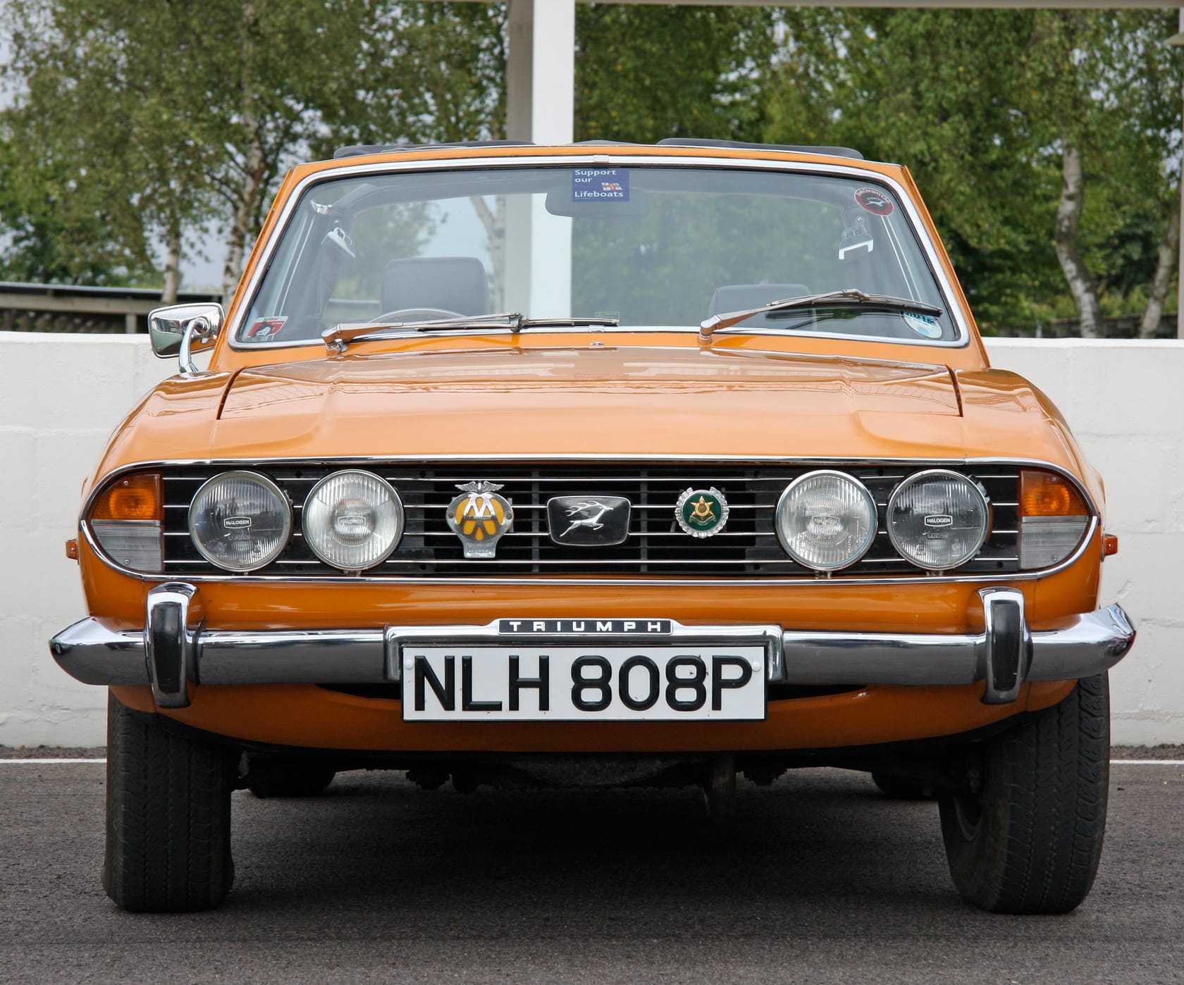 An orange 1976 Triumph Stag Mk2 with a UK registration, seen head-on with its hood up