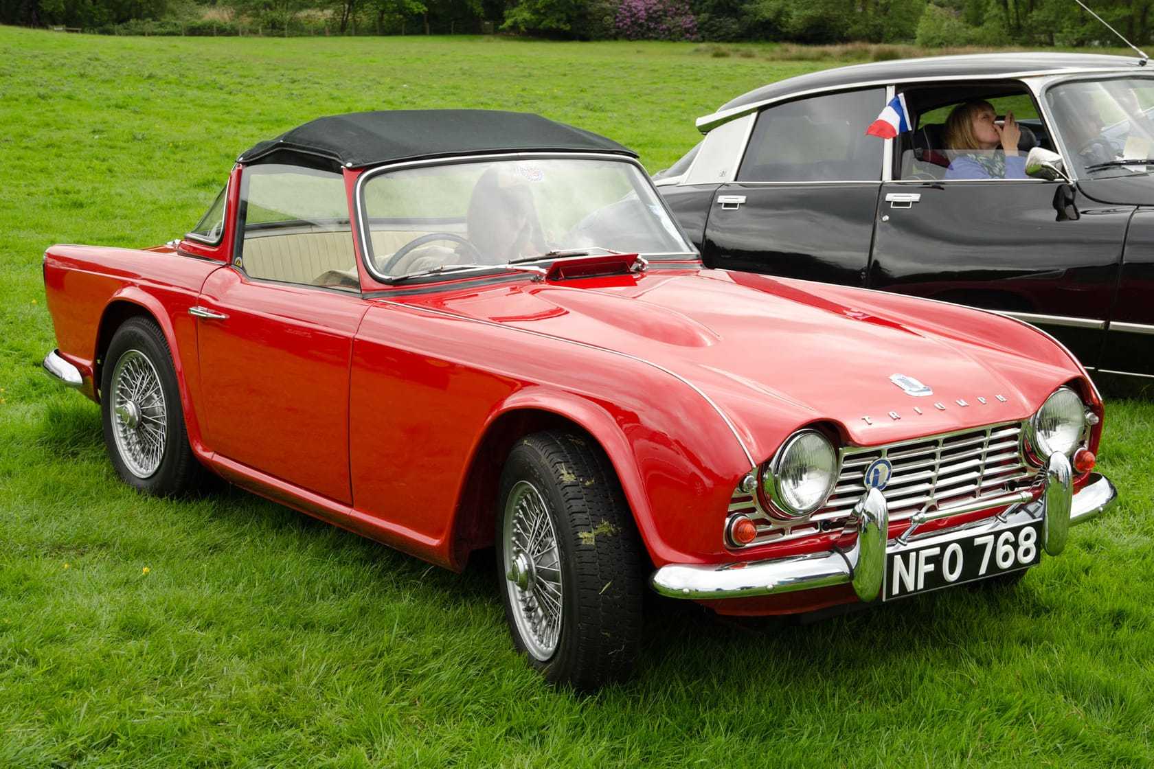 A red 1962 Triumph TR4 with a black hood, wire wheels and a UK registration on a show field