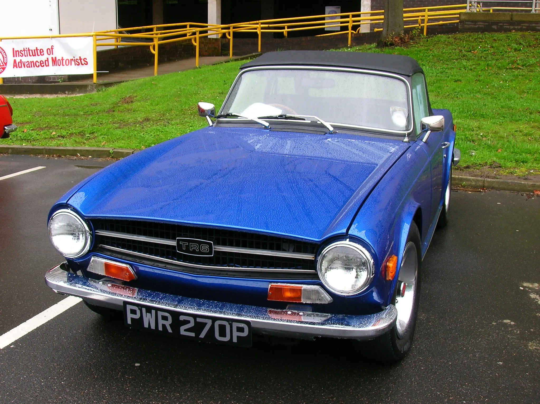 A blue Triumph TR6 roadster, top down, front three-quarter view on a road