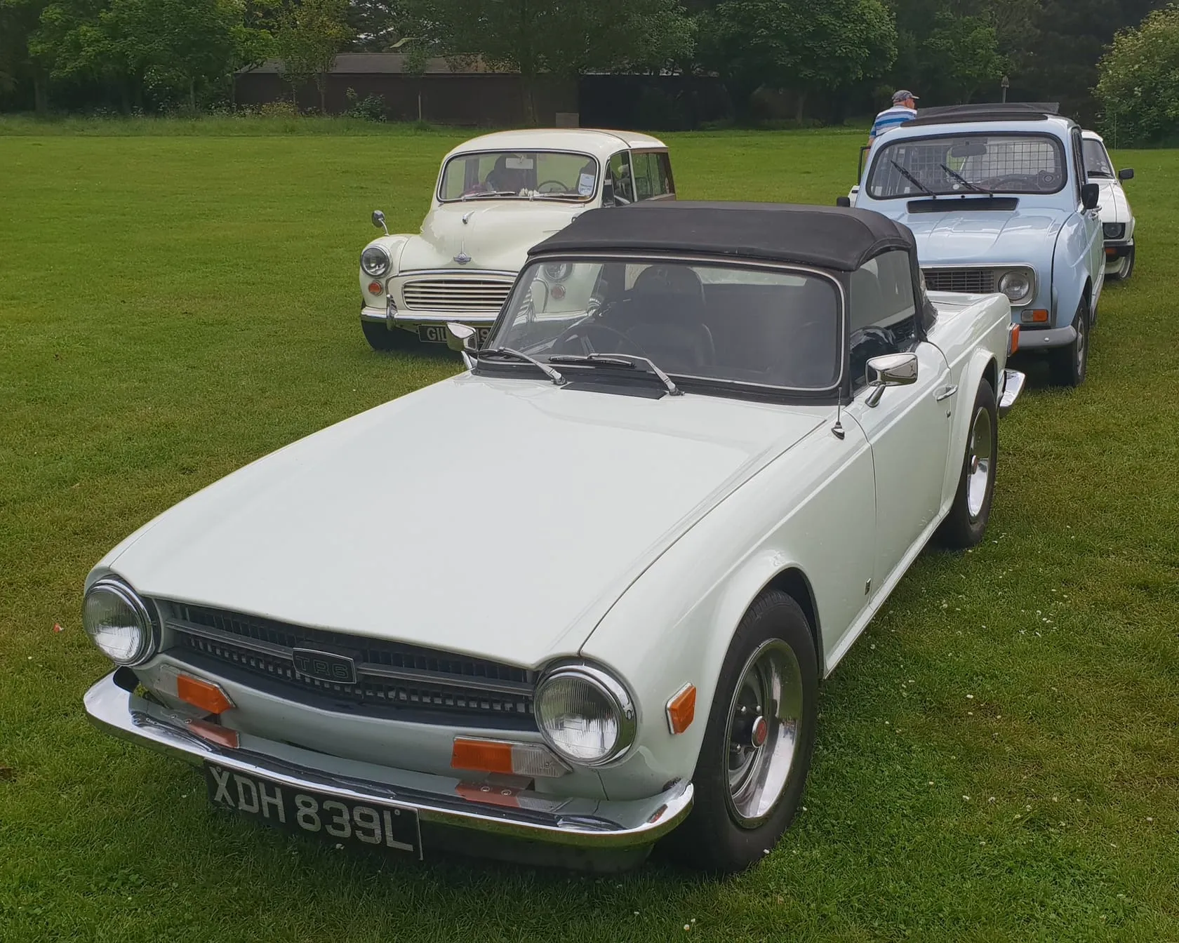 A white Triumph TR6 roadster with the soft top raised, front three-quarter view on grass at a classic car show, UK registration XDH 839L