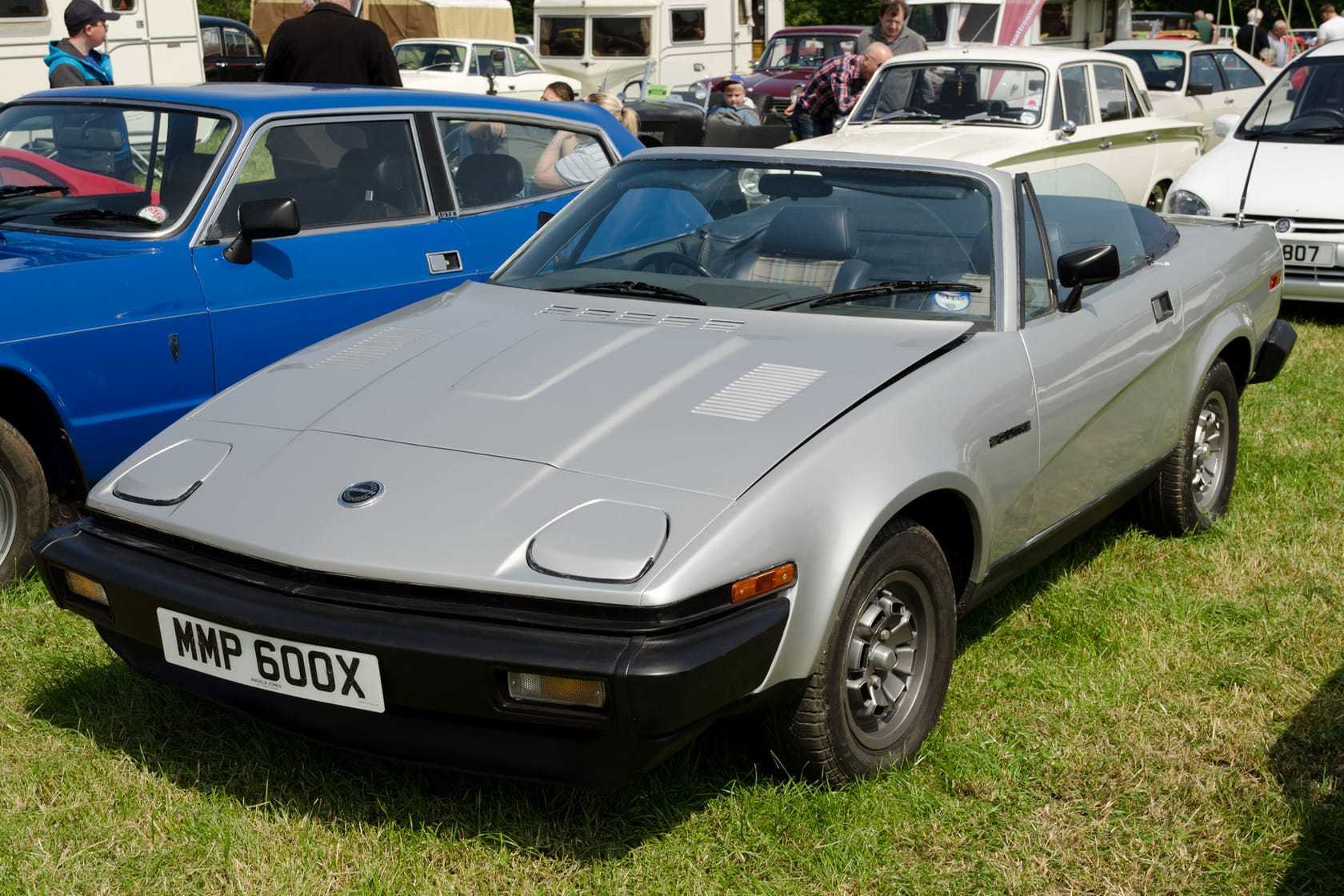 A silver 1981 Triumph TR7 convertible with its hood down at a classic car show, UK registration MMP 600X