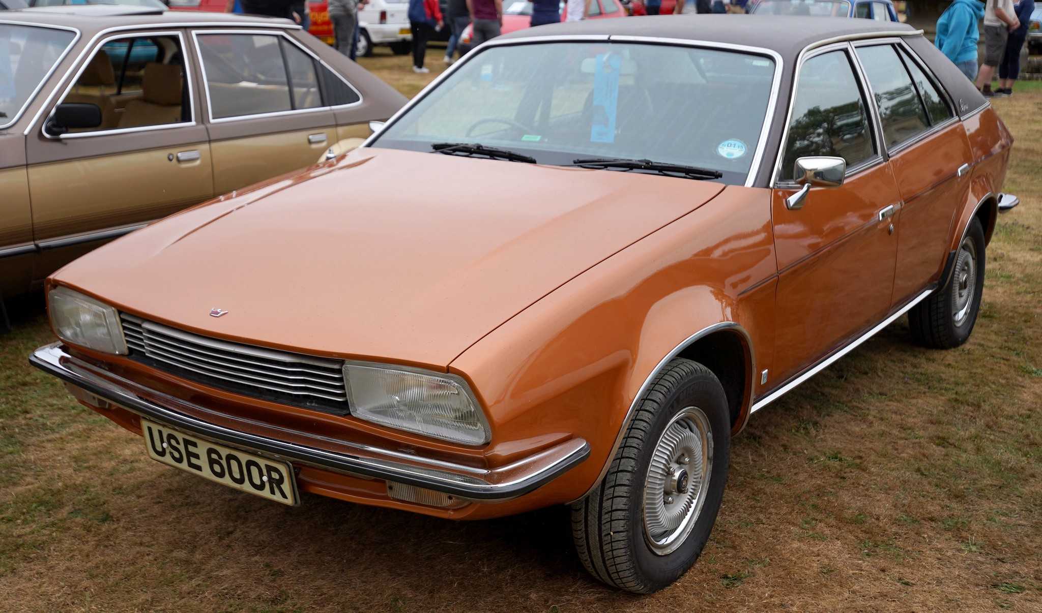 A bright orange Austin Princess wedge saloon (1976-77) with black vinyl roof at an outdoor classic car show, front three-quarter view