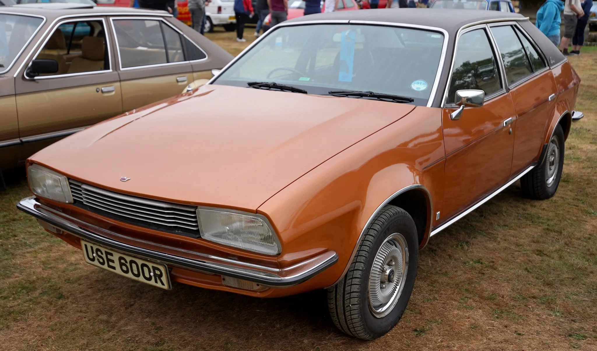 A bright orange Austin Princess wedge saloon (R plate, 1976-77) with black vinyl roof, front three-quarter view at an outdoor classic car show