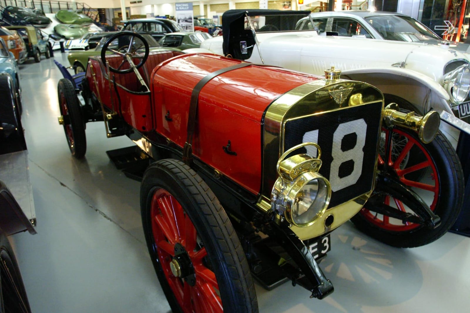 A red 1908 Austin 100hp racing car with brass radiator and race number 18, on museum display