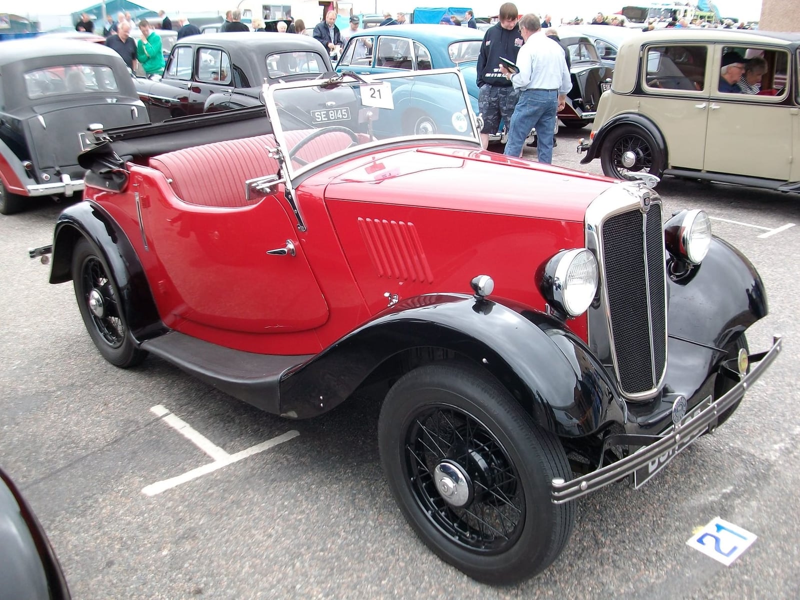 A red and black Morris Eight two-seat tourer parked on tarmac, front three-quarter view