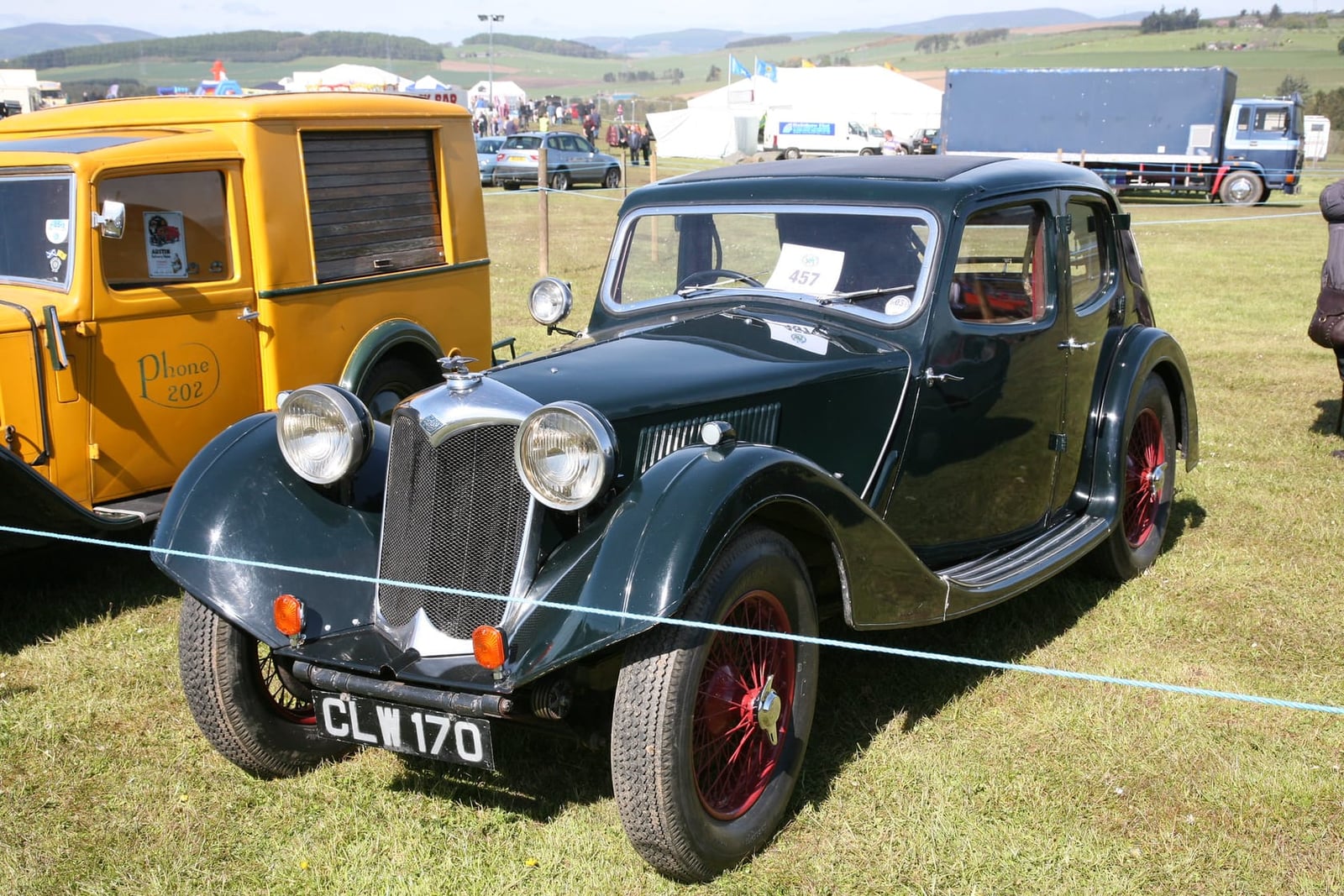 A dark green 1935 Riley Kestrel fastback saloon on grass at a classic vehicle show, front three-quarter view, UK registration CLW 170