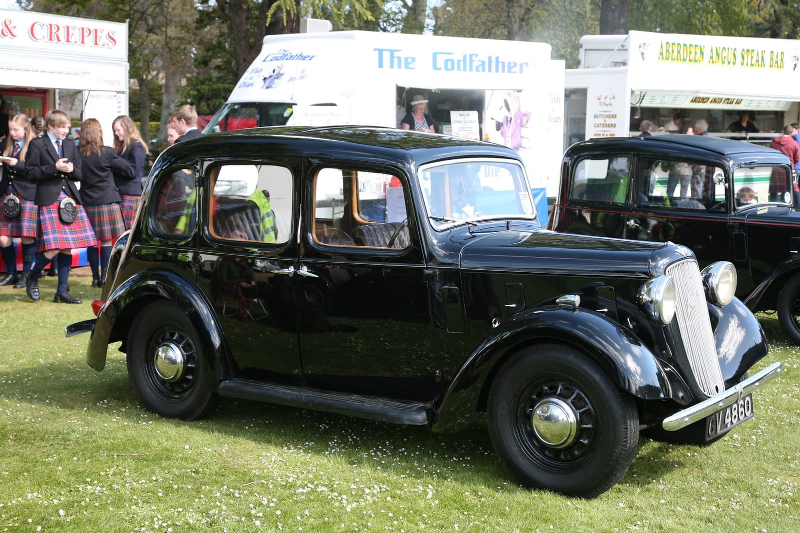A black 1936 Austin Ten Cambridge saloon on grass at a classic vehicle show, side view