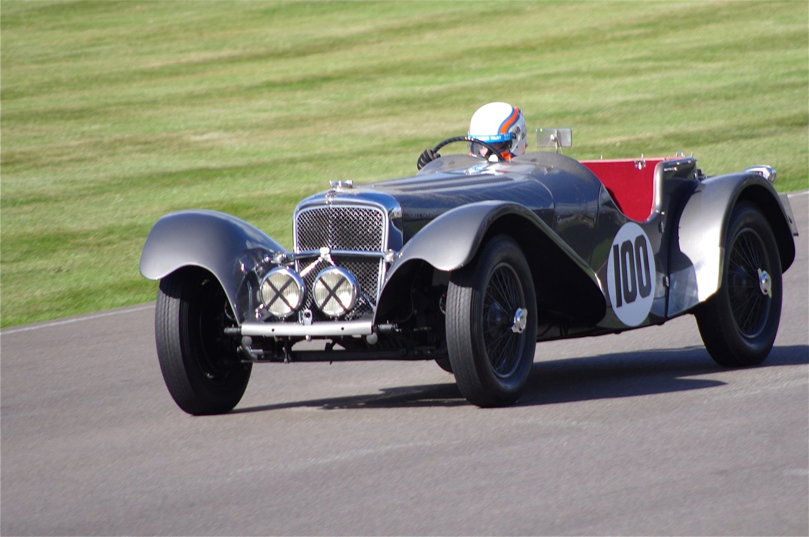 A silver SS Jaguar 100 racing on a circuit, front three-quarter view, race number 100