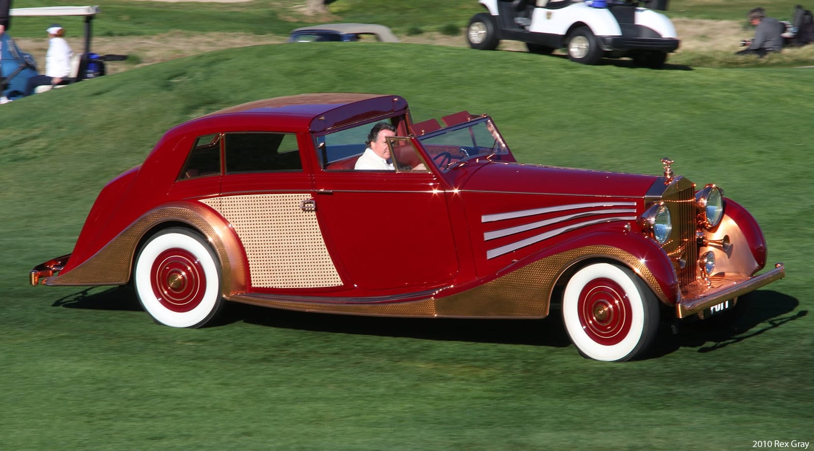 A red and gold 1937 Rolls-Royce Phantom III sedanca de ville at a concours