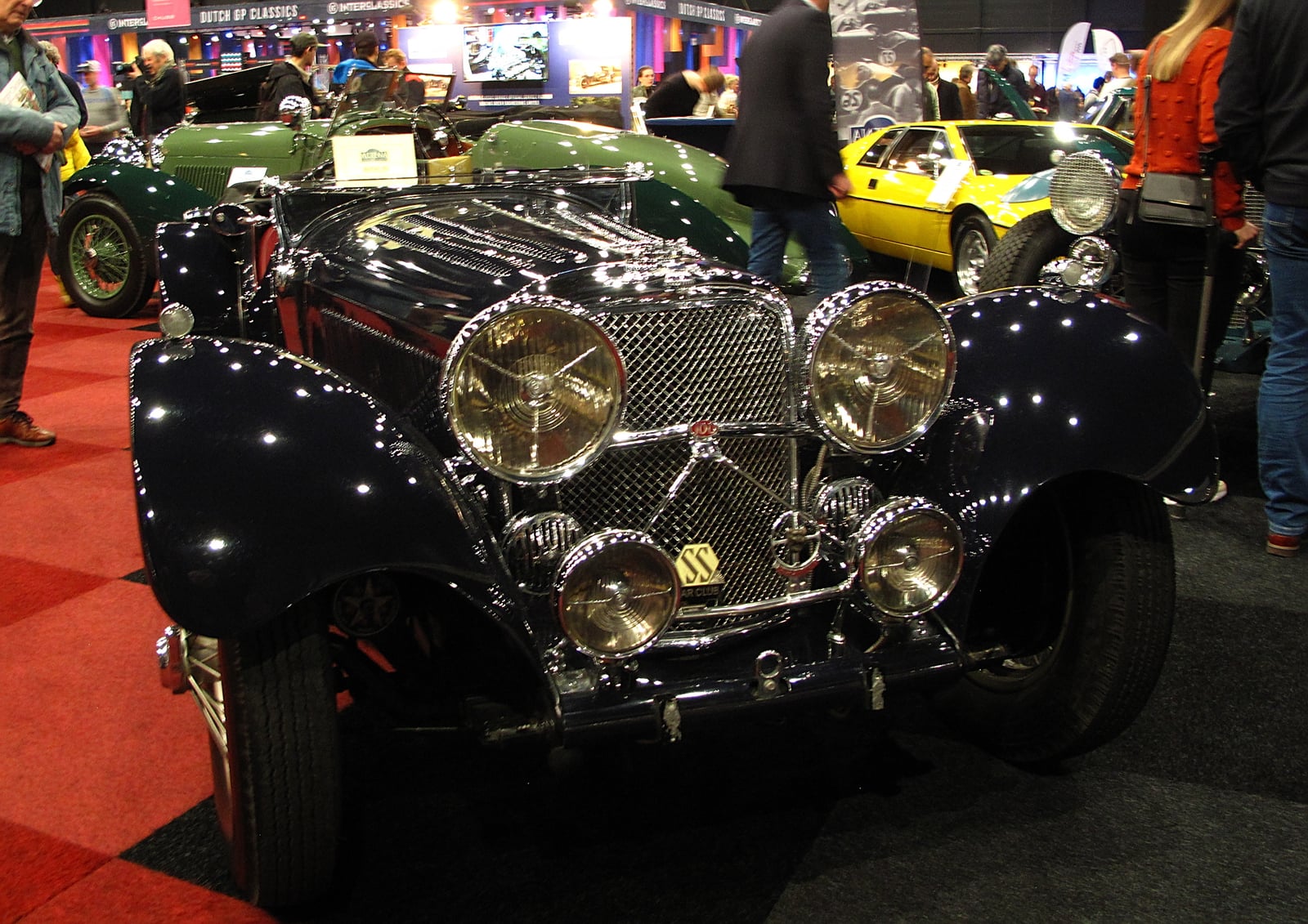 A dark SS Jaguar 100 with its bonnet open, showing the six-cylinder engine