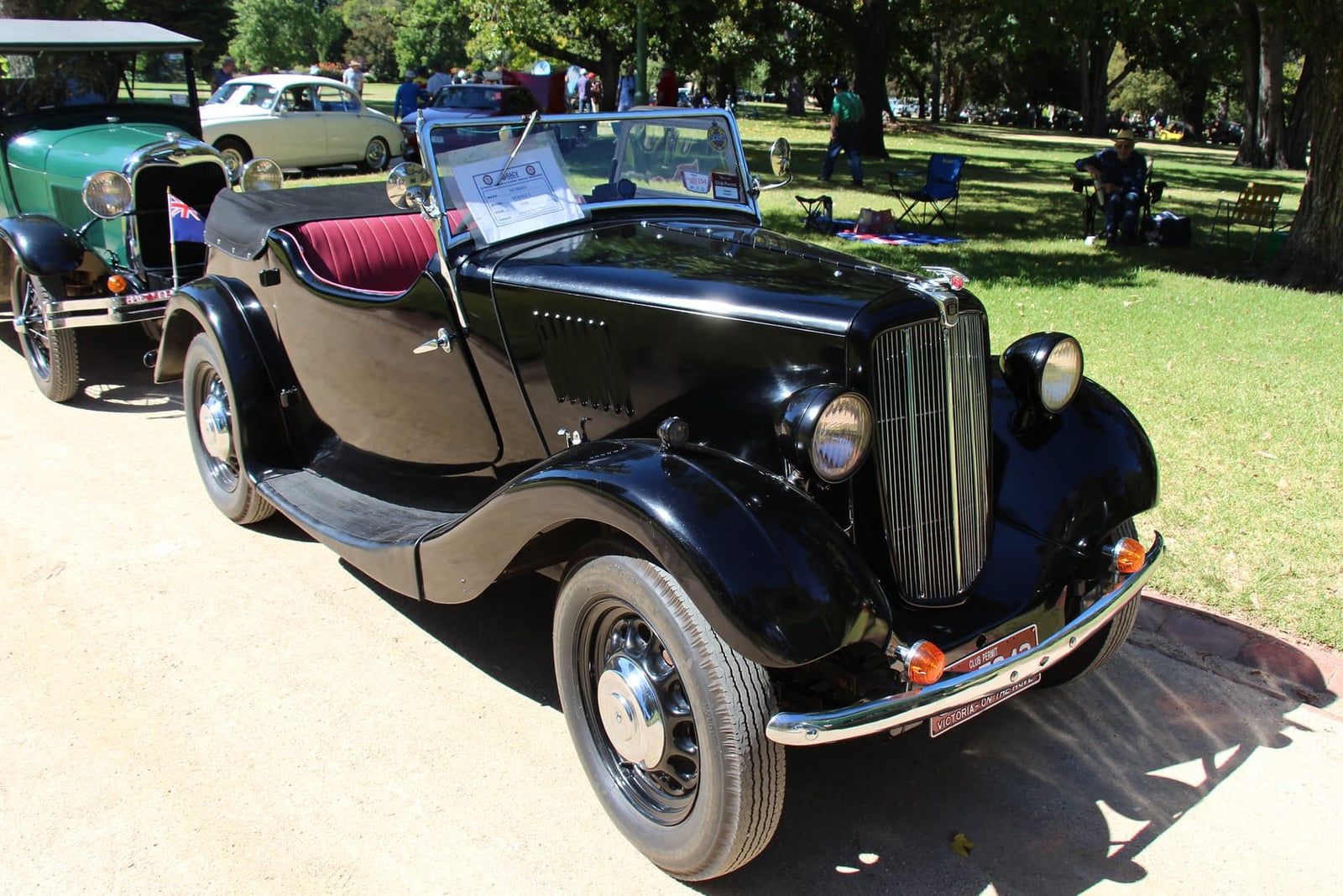 A green and black Morris Eight Series II saloon on grass at a classic vehicle show, front three-quarter view