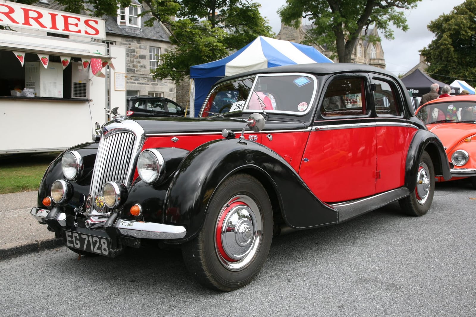 A red and black 1946 Riley RMA saloon at a summer fair, front three-quarter view